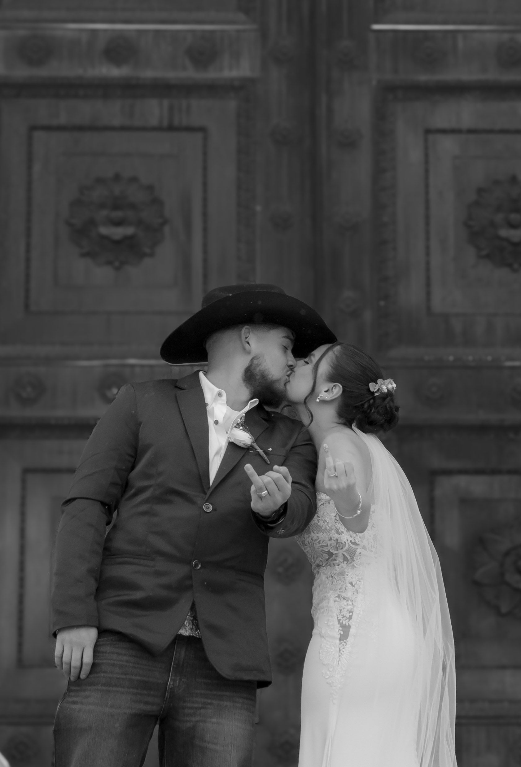 A bride and groom are kissing in front of a wooden door.