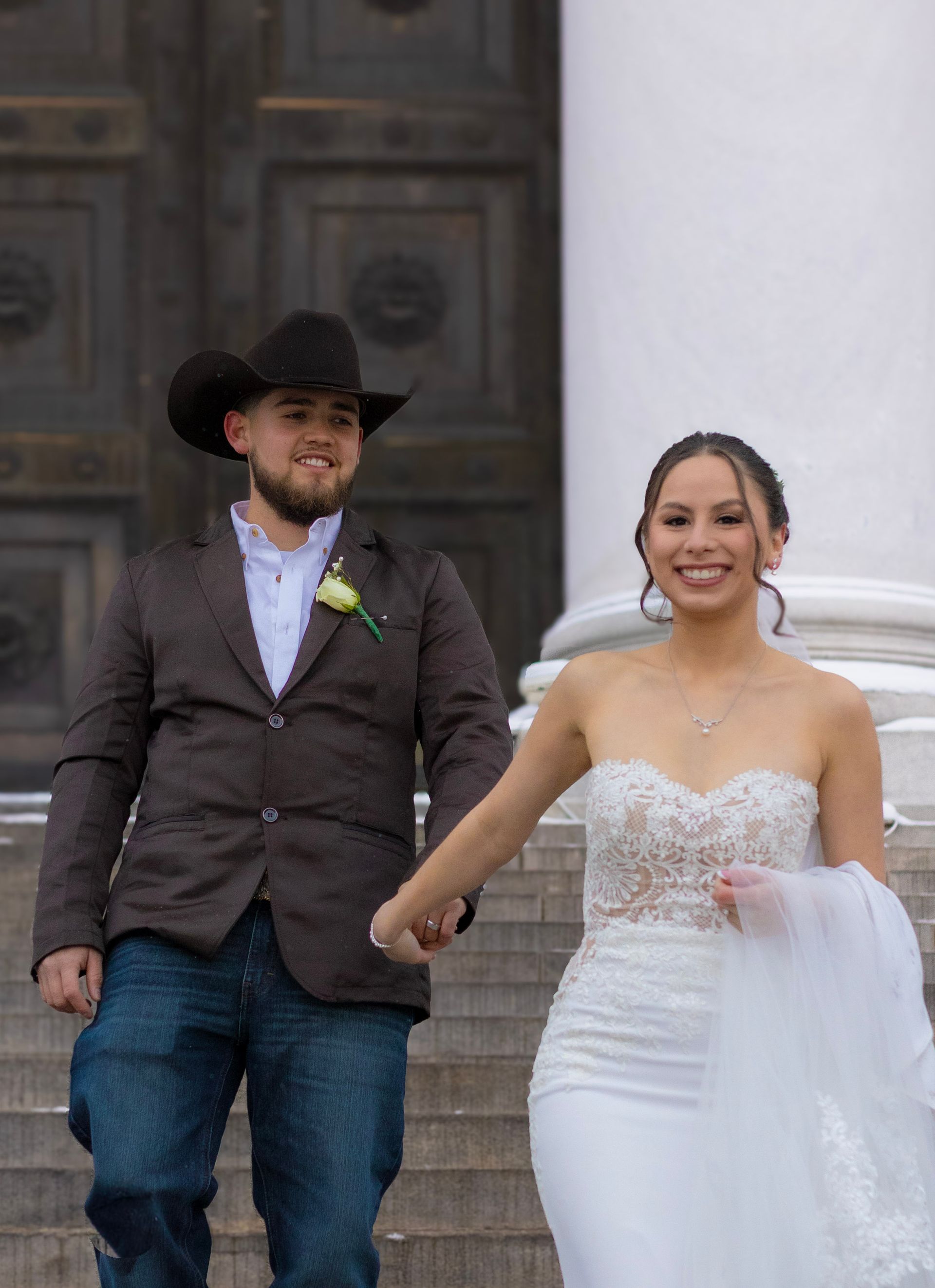 A bride and groom are walking down the stairs holding hands.