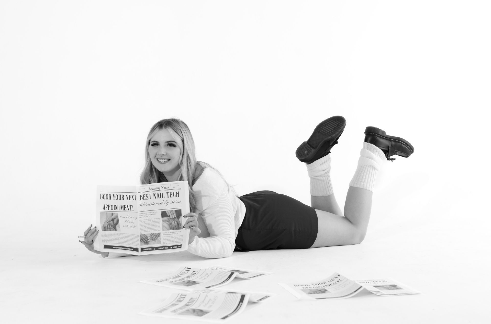 A woman is laying on the floor holding a newspaper.