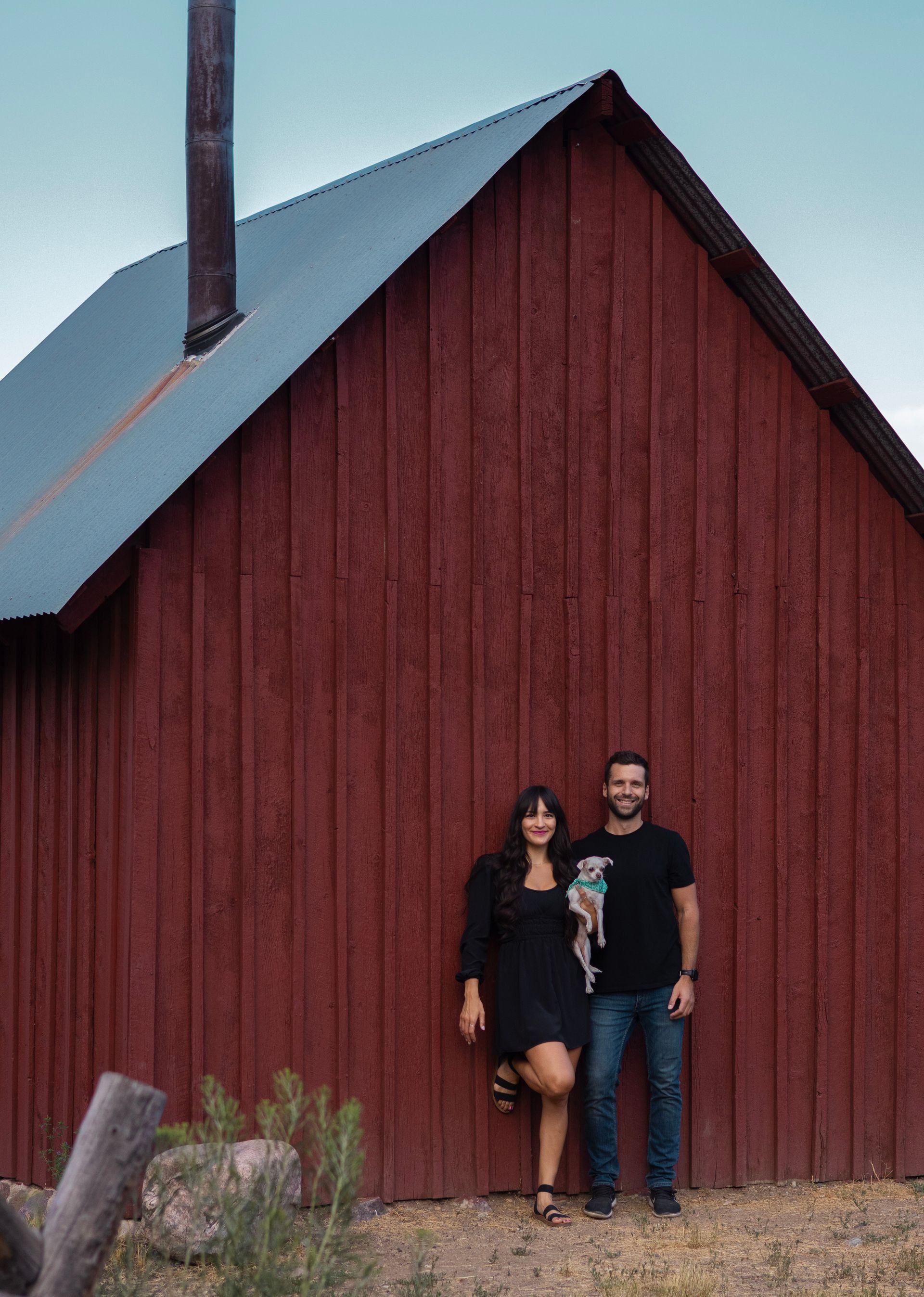 A man and a woman are standing in front of a red barn.