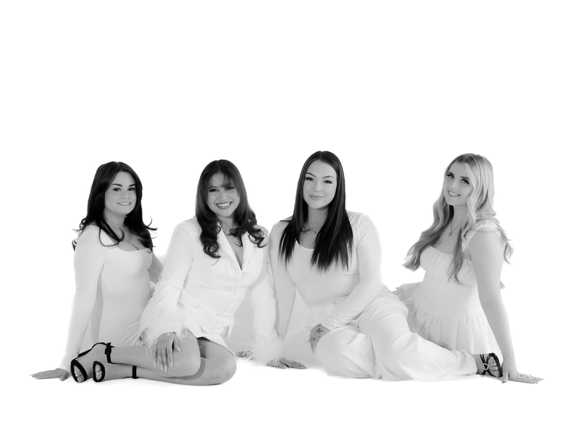 A group of four women are sitting on the floor in a black and white photo.
