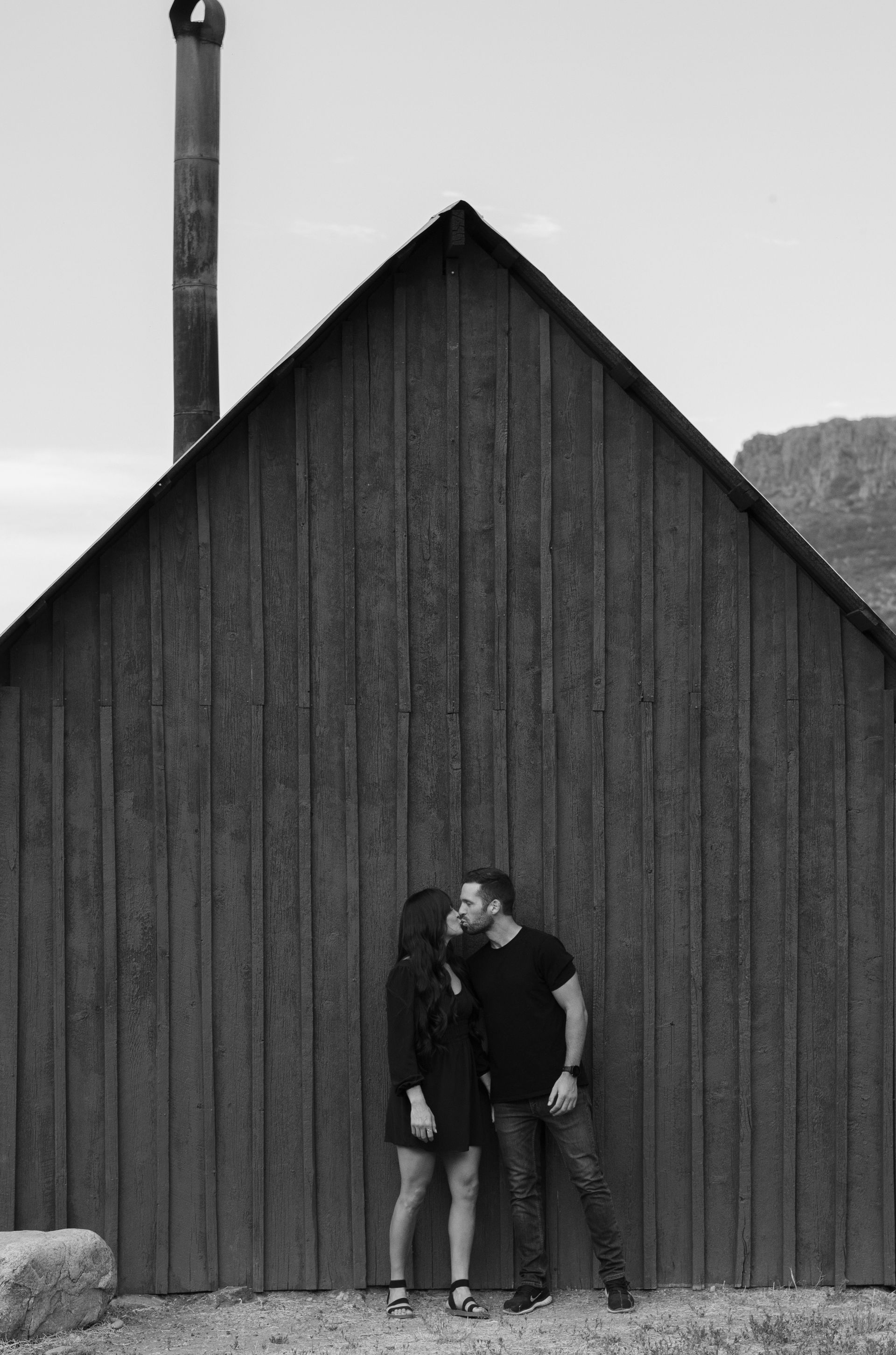 A man and a woman are kissing in front of a wooden building.