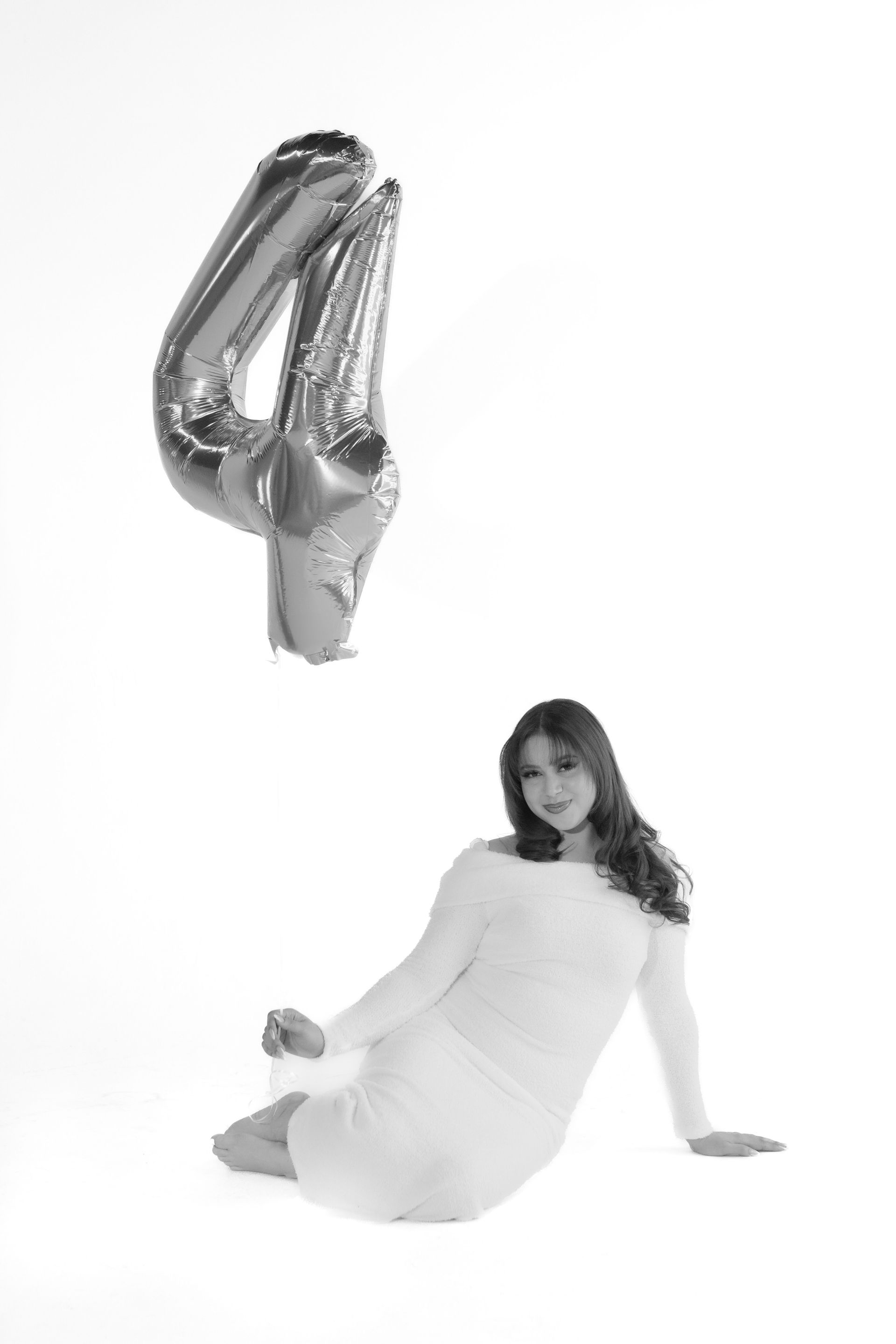 A woman is sitting on the floor next to a silver number four balloon.
