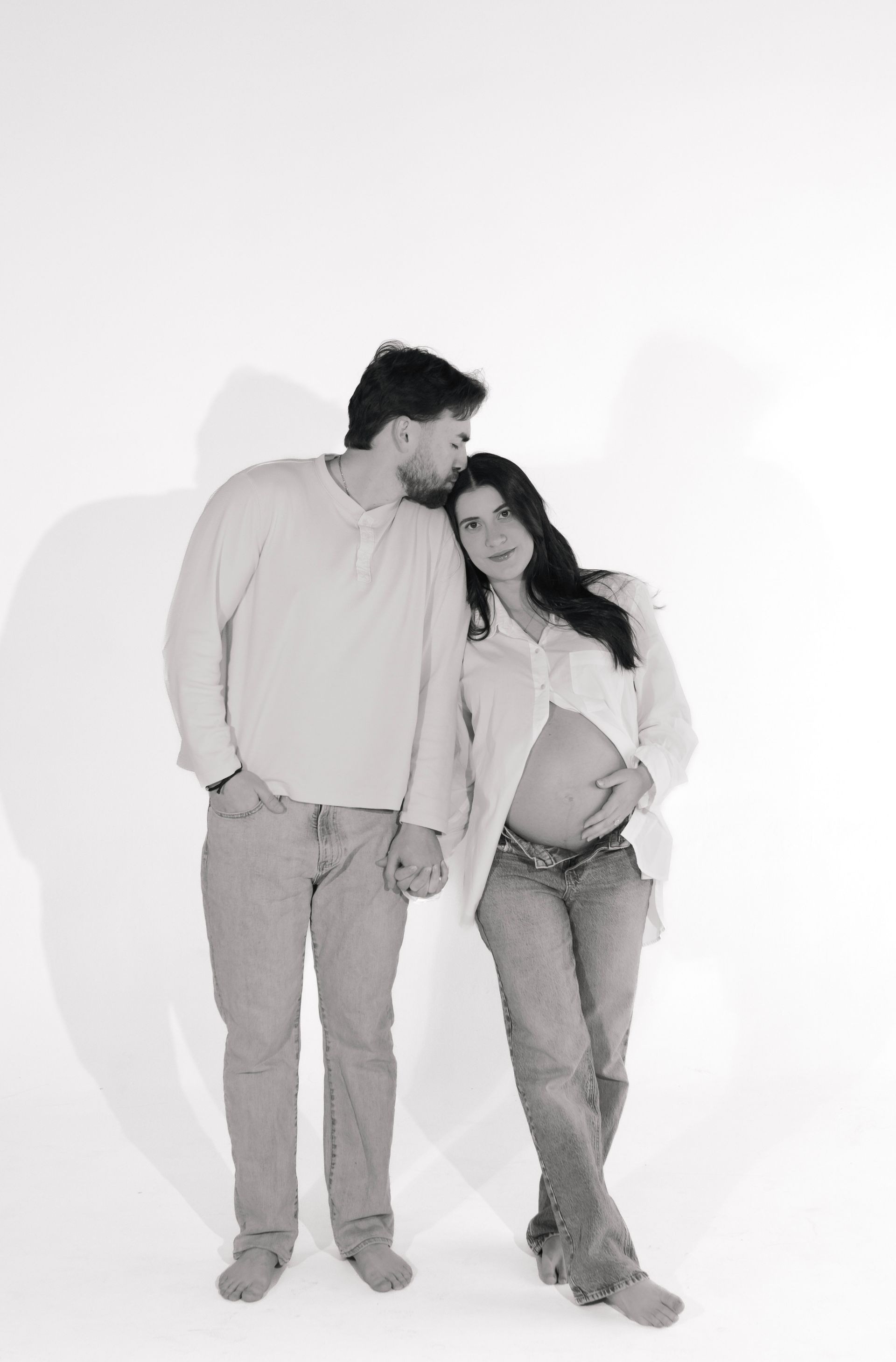 A man is kissing a pregnant woman on the cheek in a black and white photo.