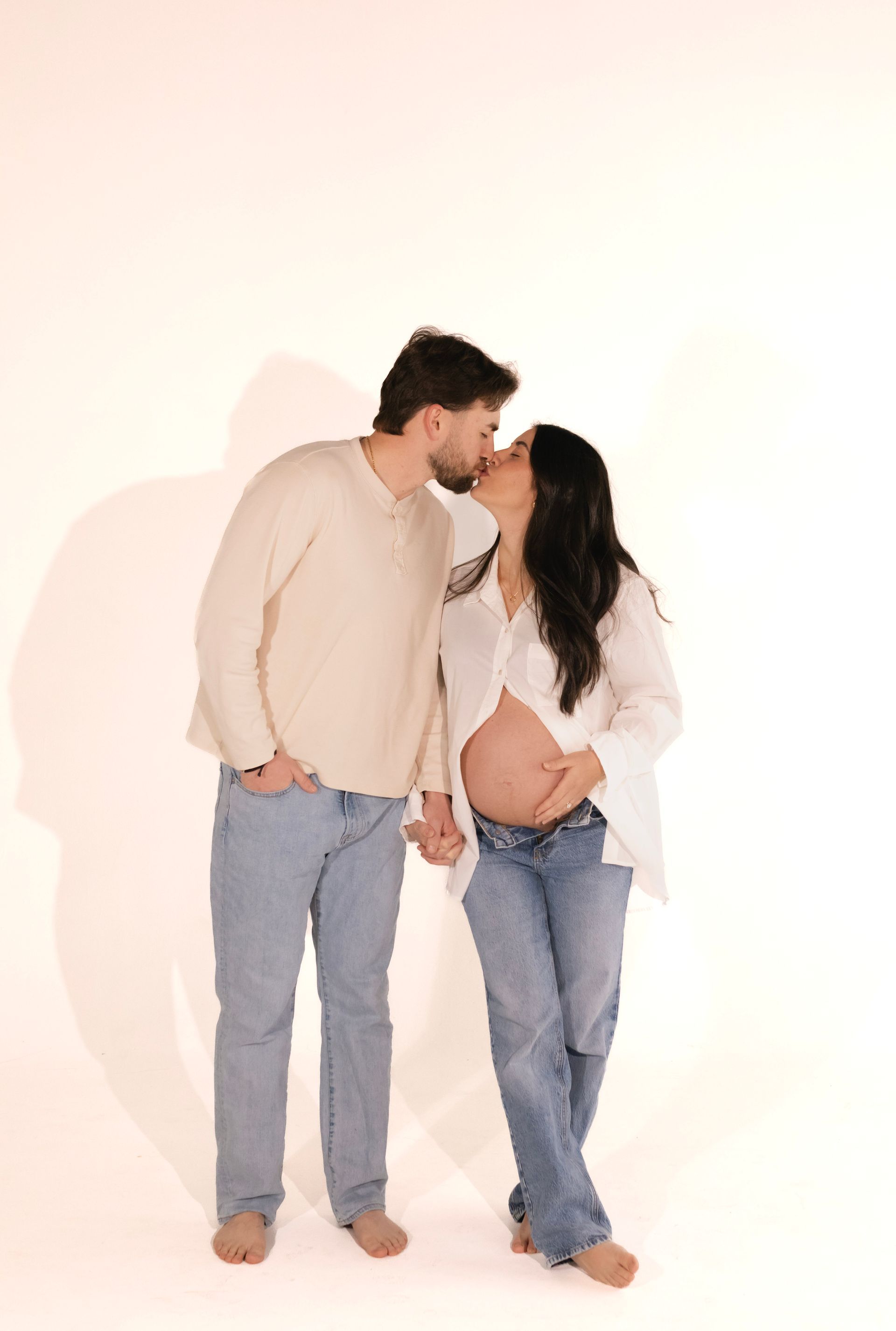 A man and a pregnant woman are kissing and holding hands.