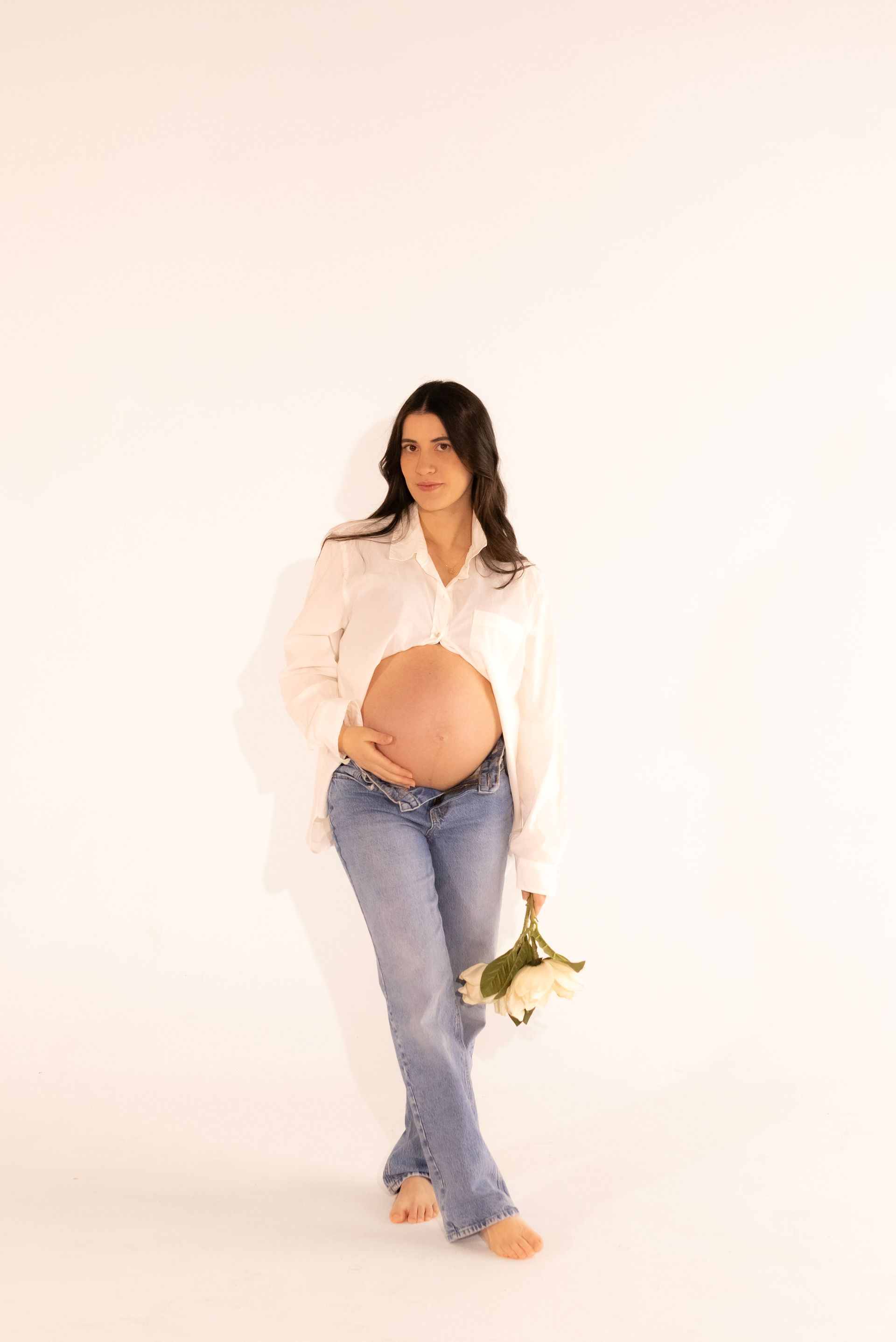 A pregnant woman in a white shirt and jeans is holding a bouquet of flowers.
