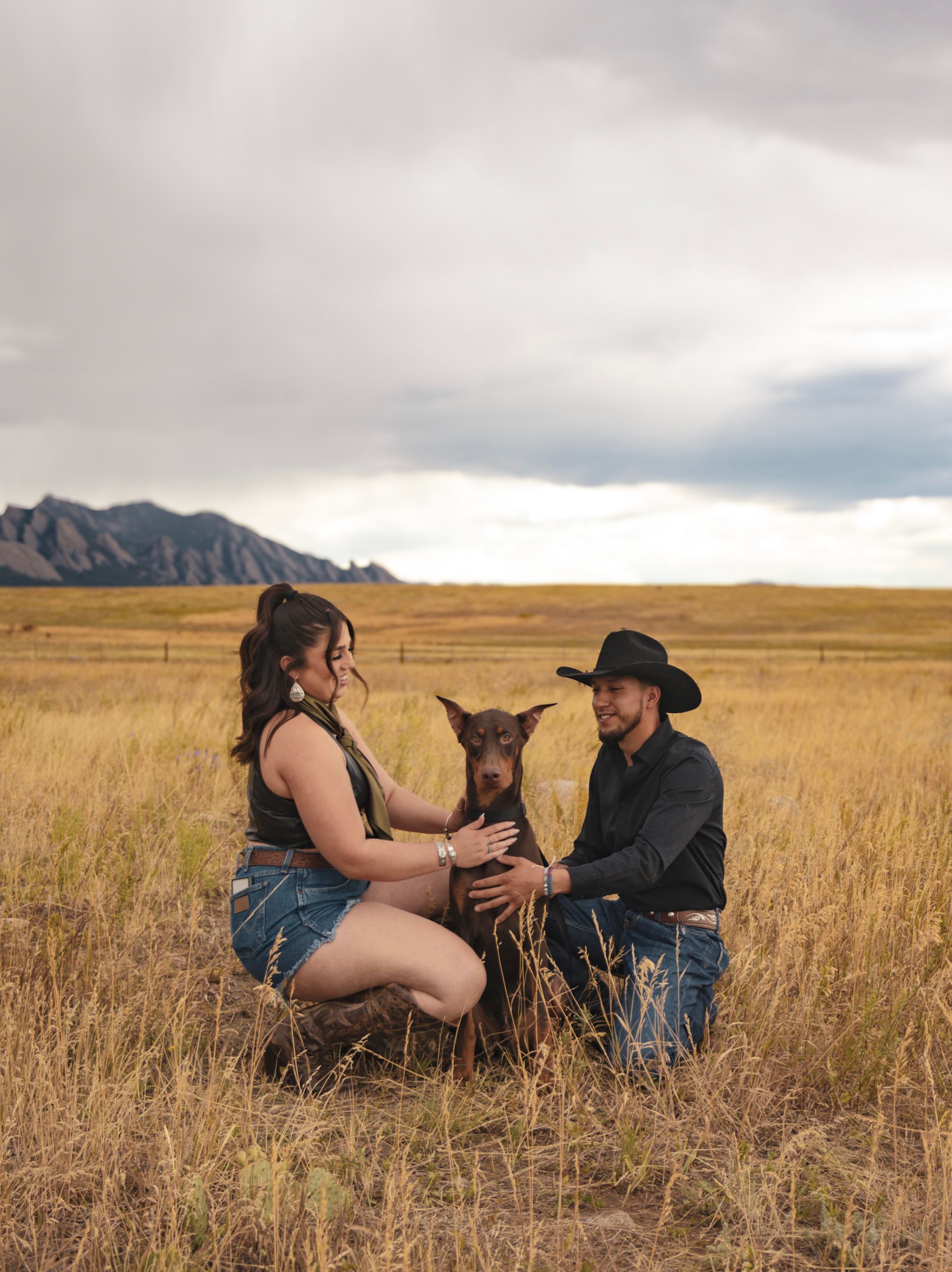 A man and a woman are kneeling in a field with a dog.