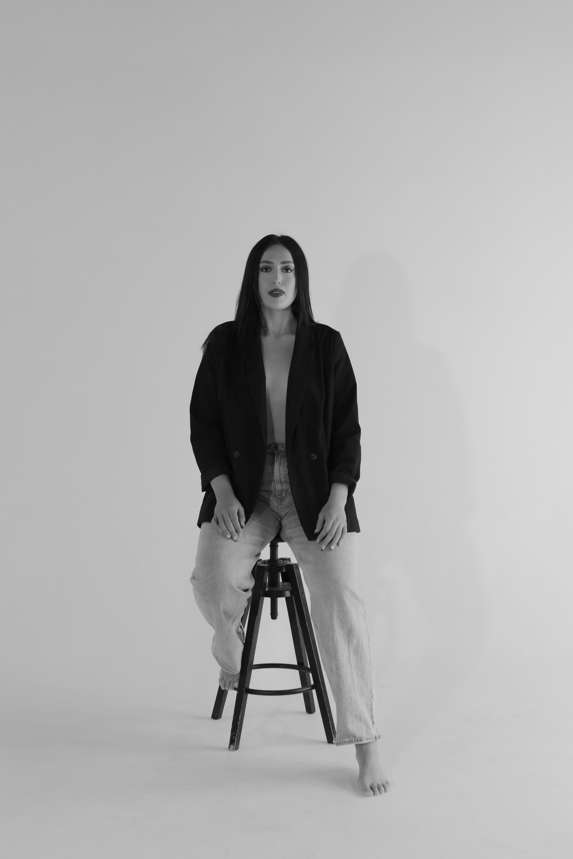 A woman is sitting on a stool in a black and white photo.