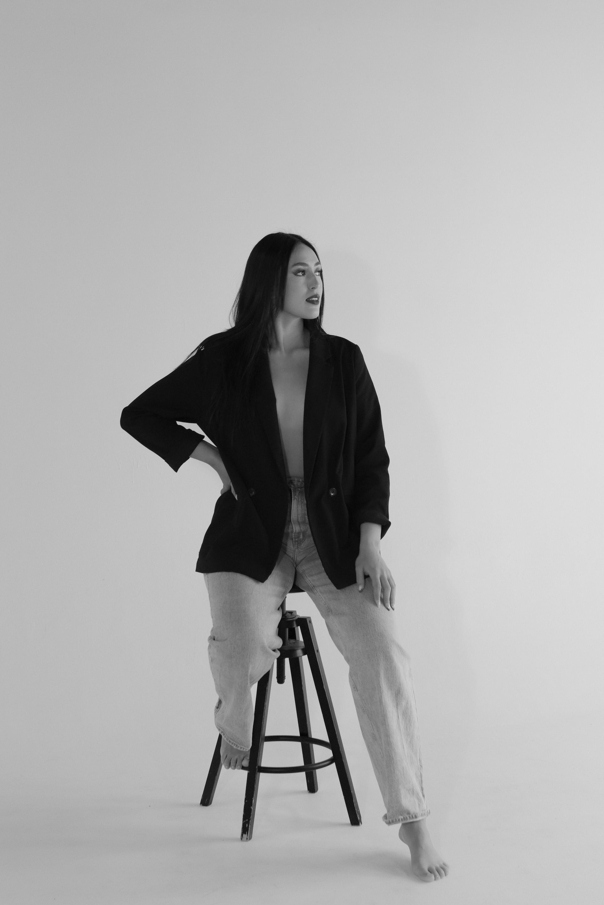 A black and white photo of a woman sitting on a stool.