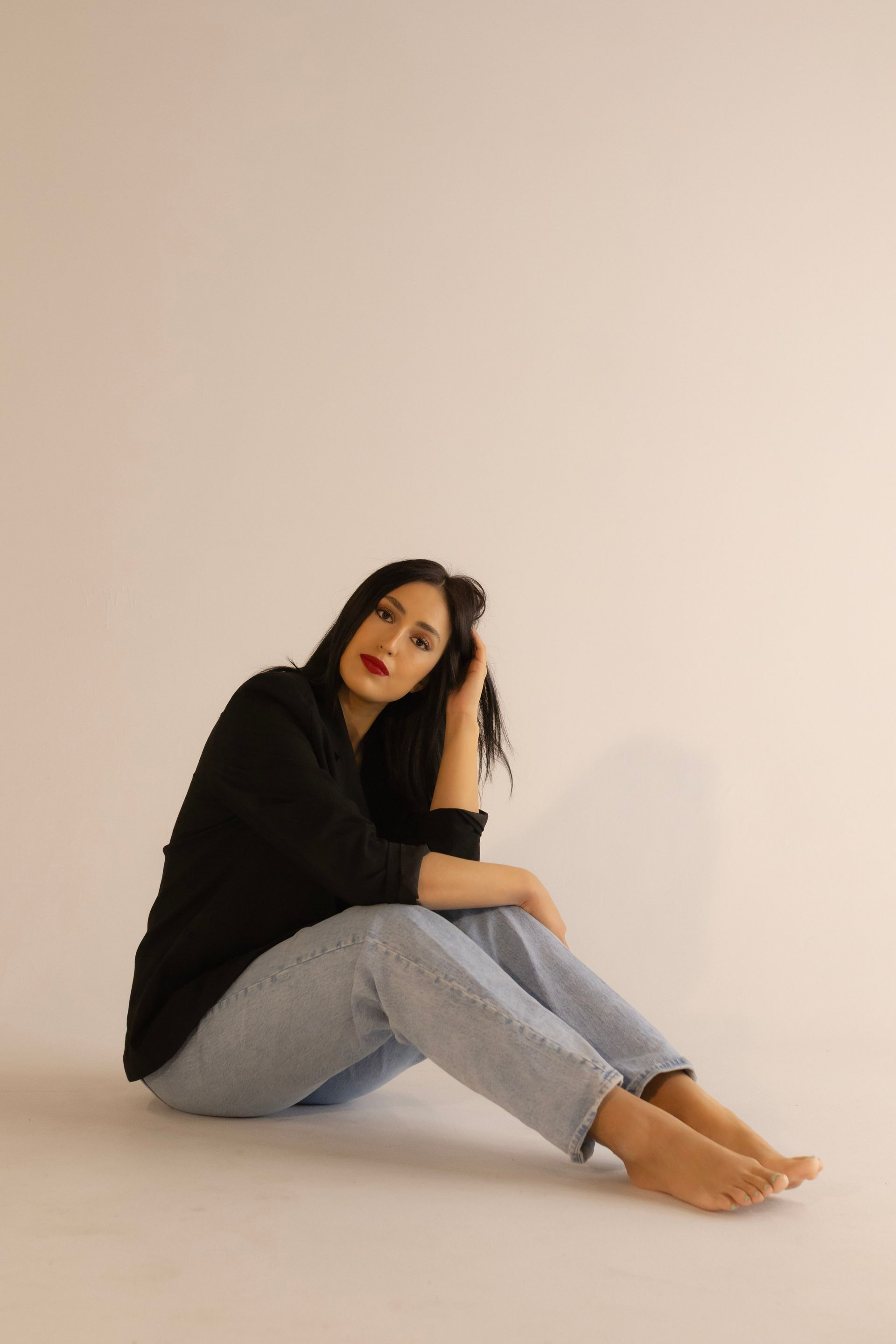 A woman in a black sweater and blue jeans is sitting on the floor.