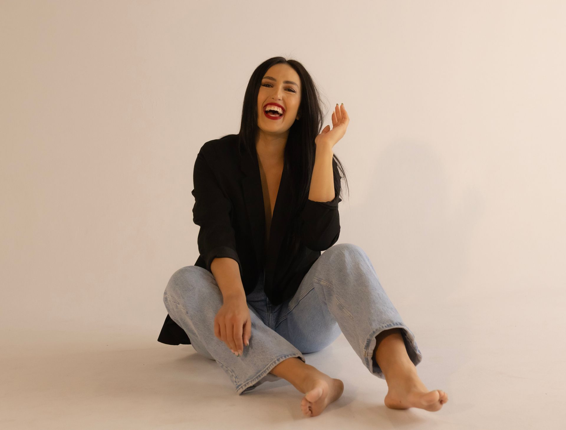 A woman is sitting on the floor with her legs crossed and laughing.