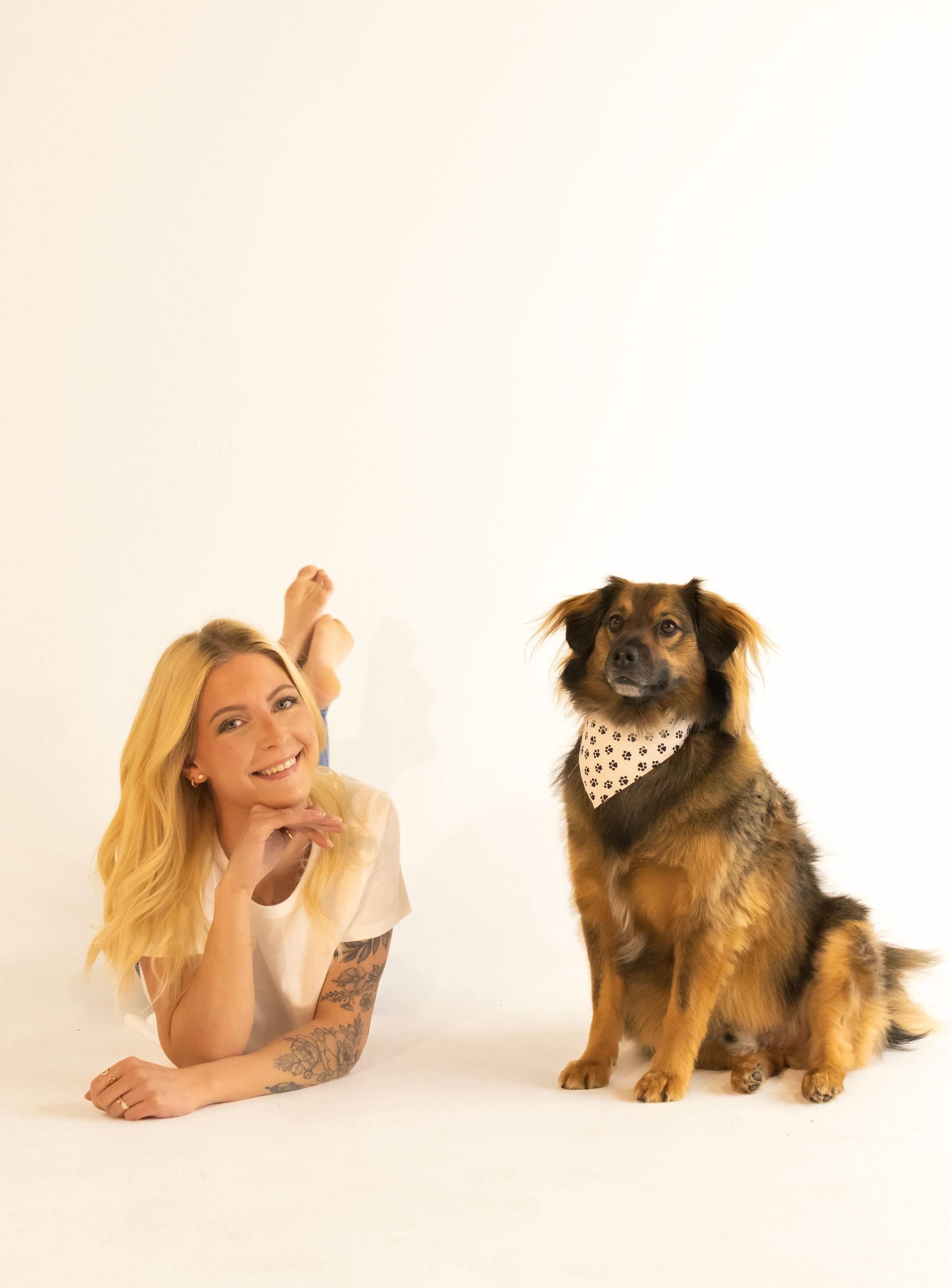 A woman is laying on the floor next to a dog wearing a bandana.