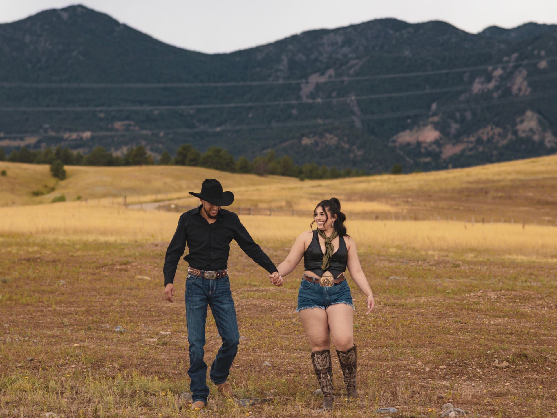 A man and a woman are walking through a field holding hands.