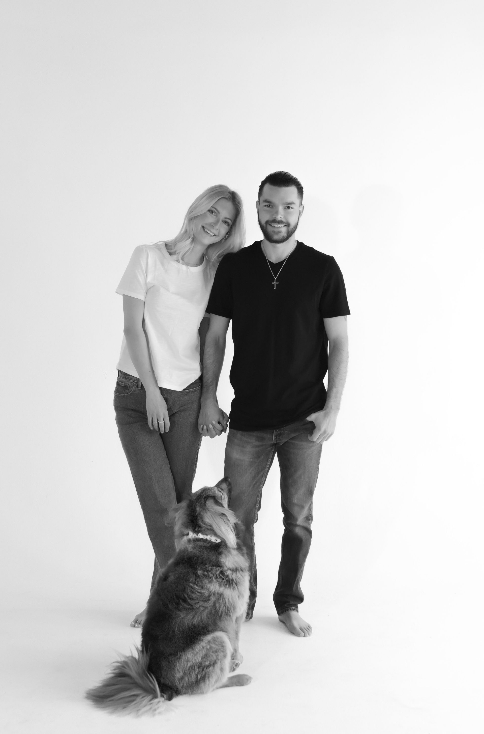A black and white photo of a man and woman standing next to a dog.