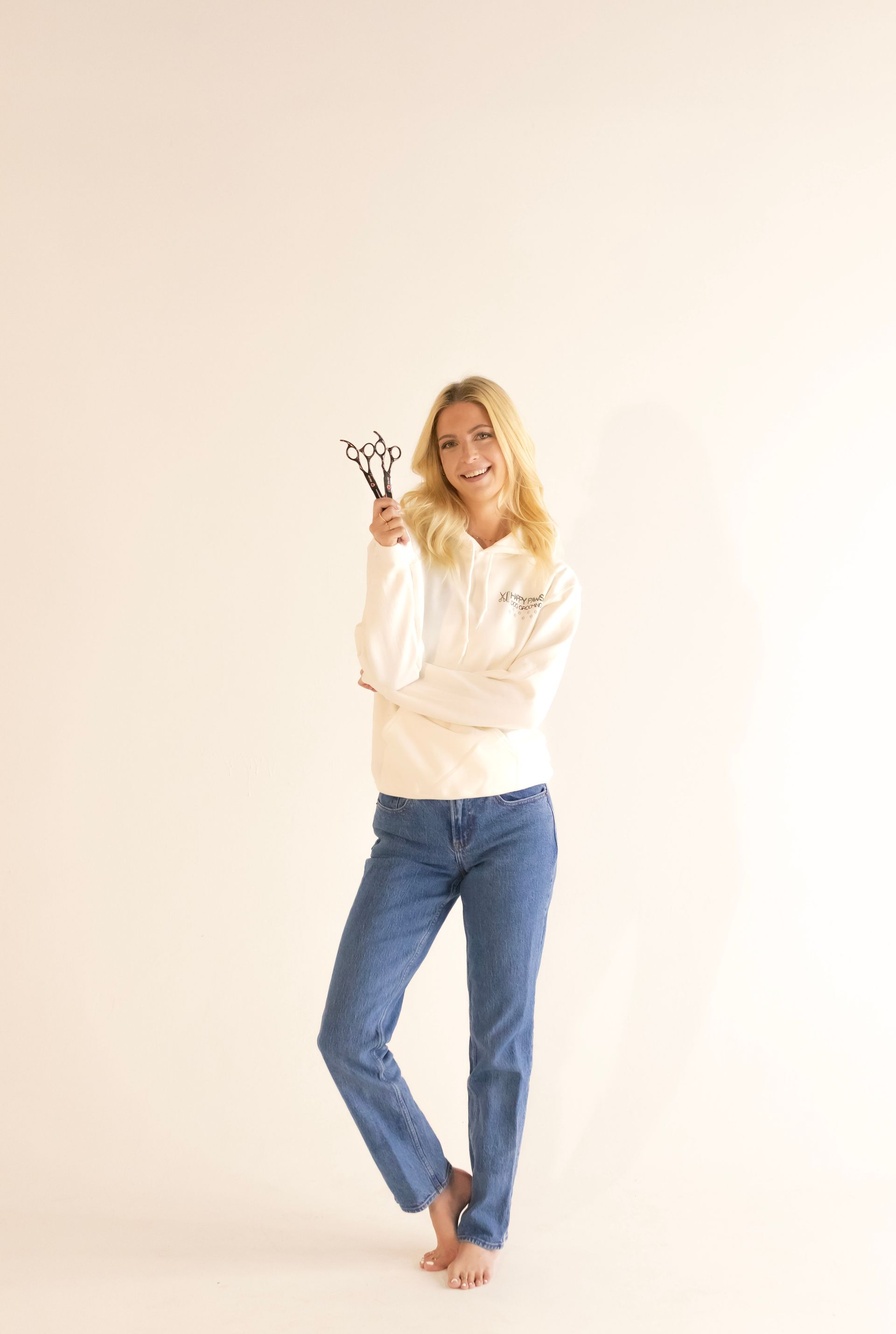 A woman in a white hoodie and blue jeans is standing in front of a white wall.