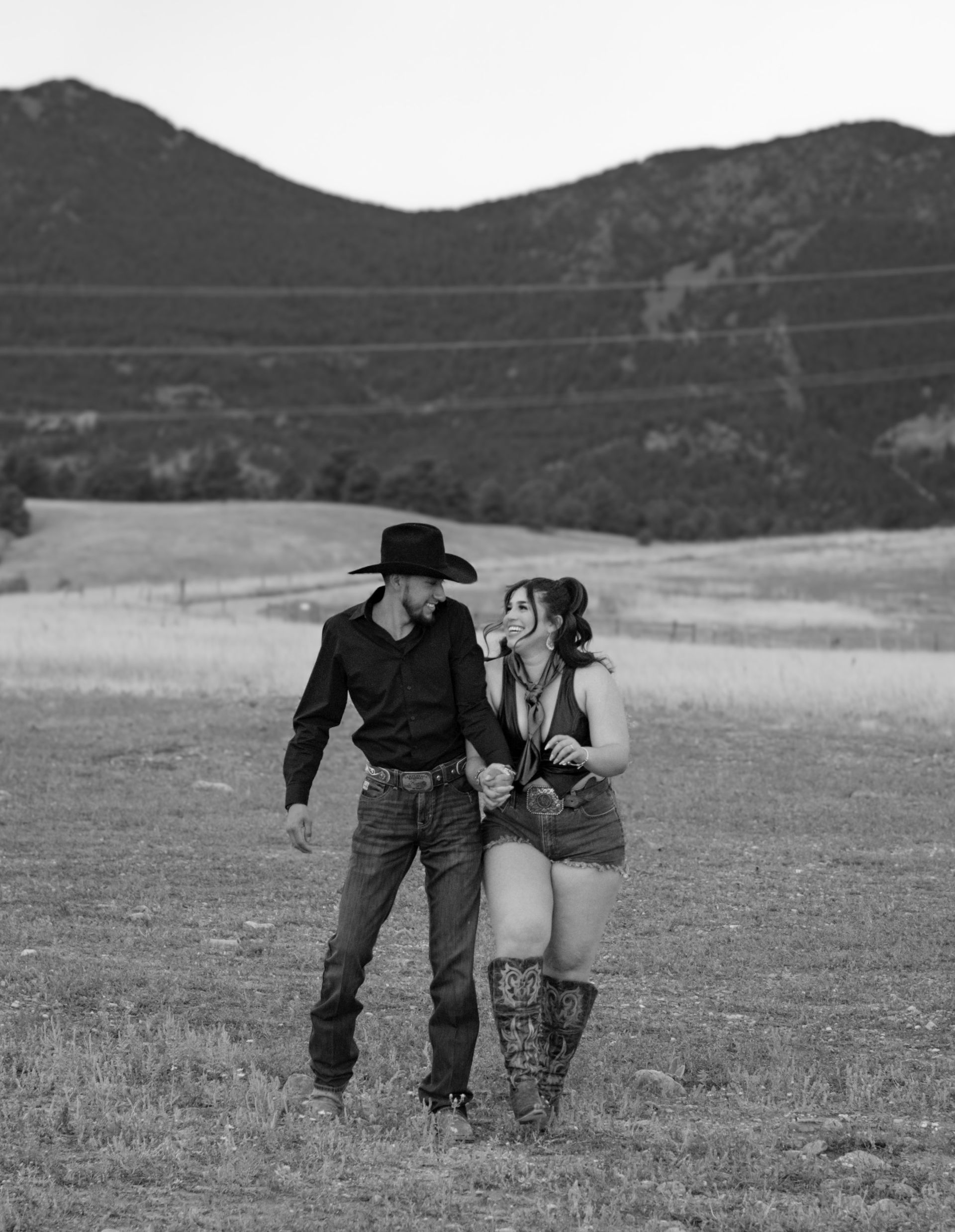A black and white photo of a man and woman holding hands in a field.