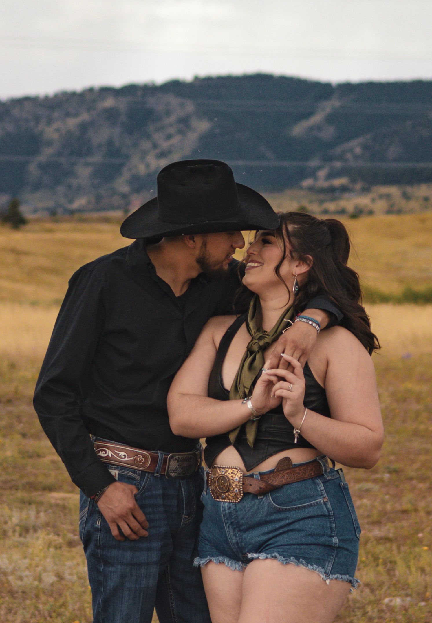 A man in a cowboy hat is kissing a woman in a field.