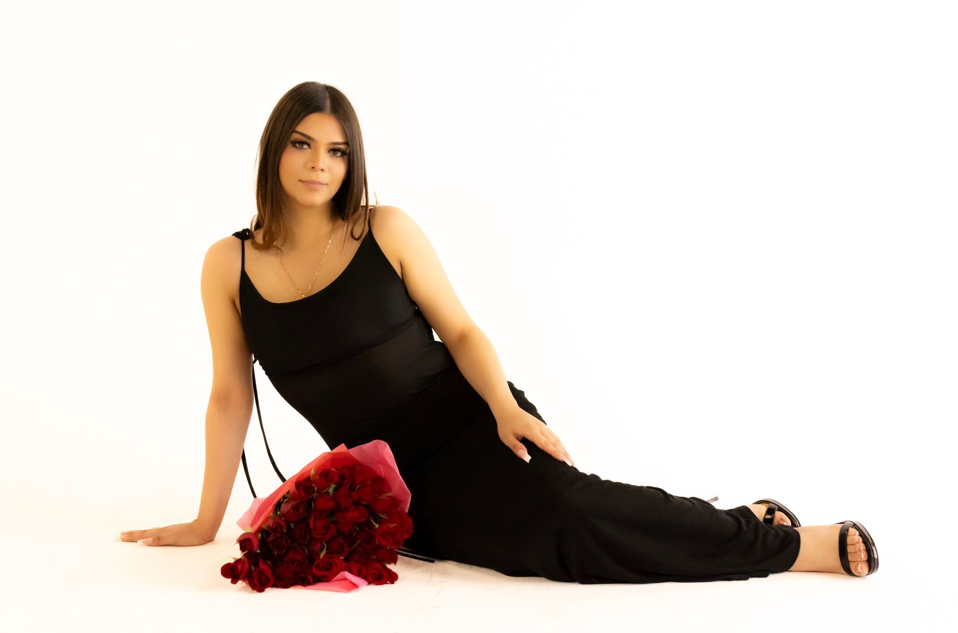 A woman in a black dress is laying on the floor with a bouquet of red roses.