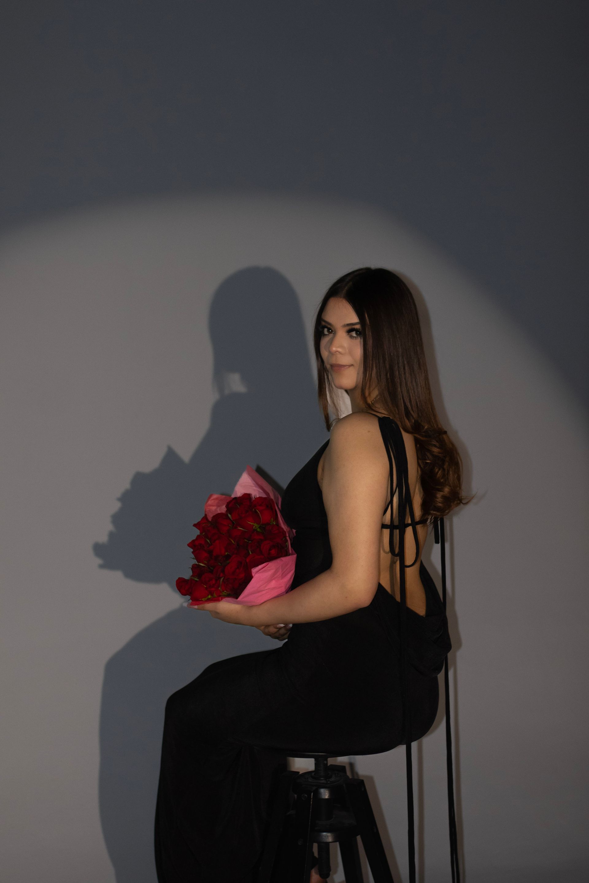 A woman in a black dress is sitting on a chair holding a bouquet of red roses.
