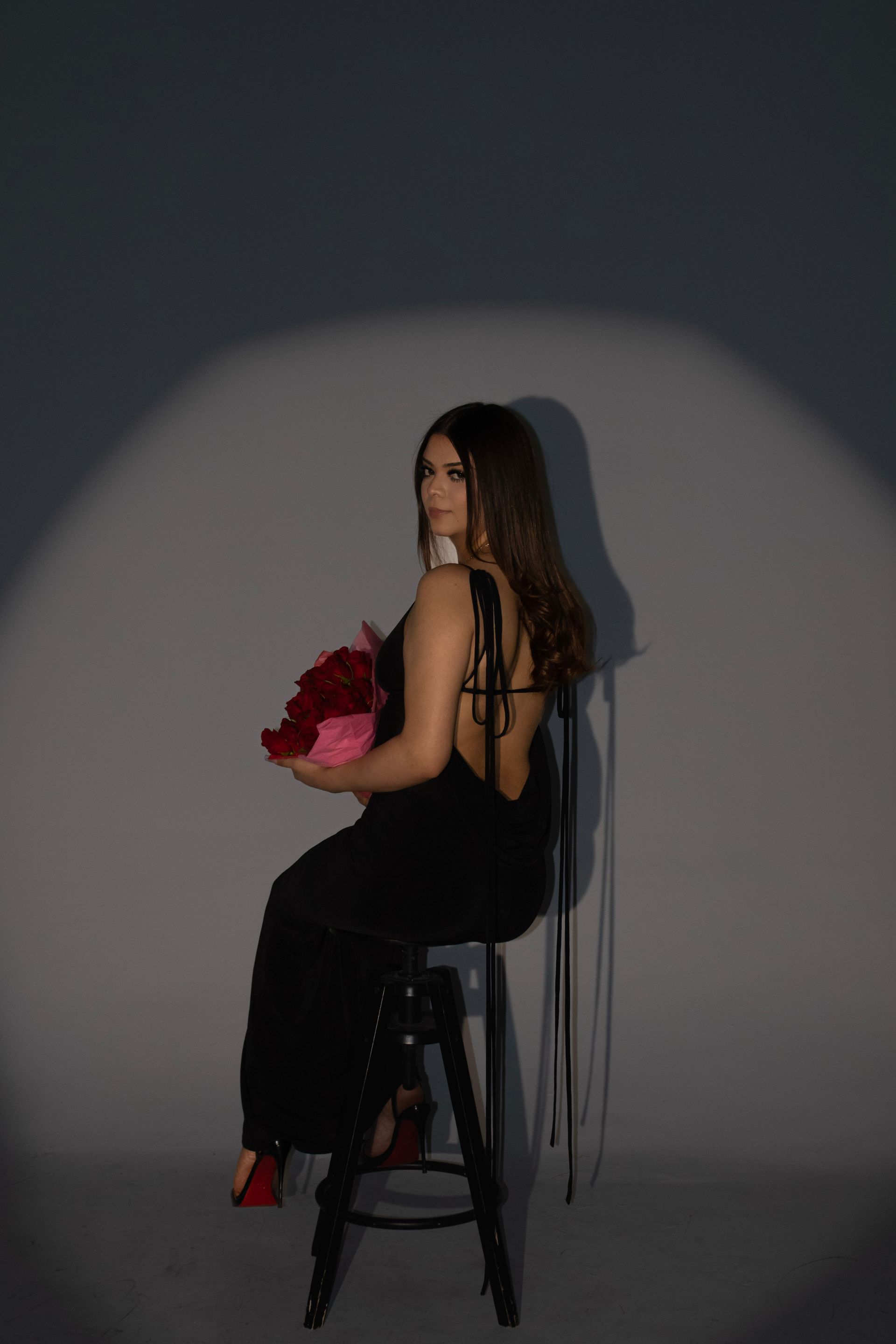 A woman in a black dress is sitting on a stool holding a bouquet of flowers.
