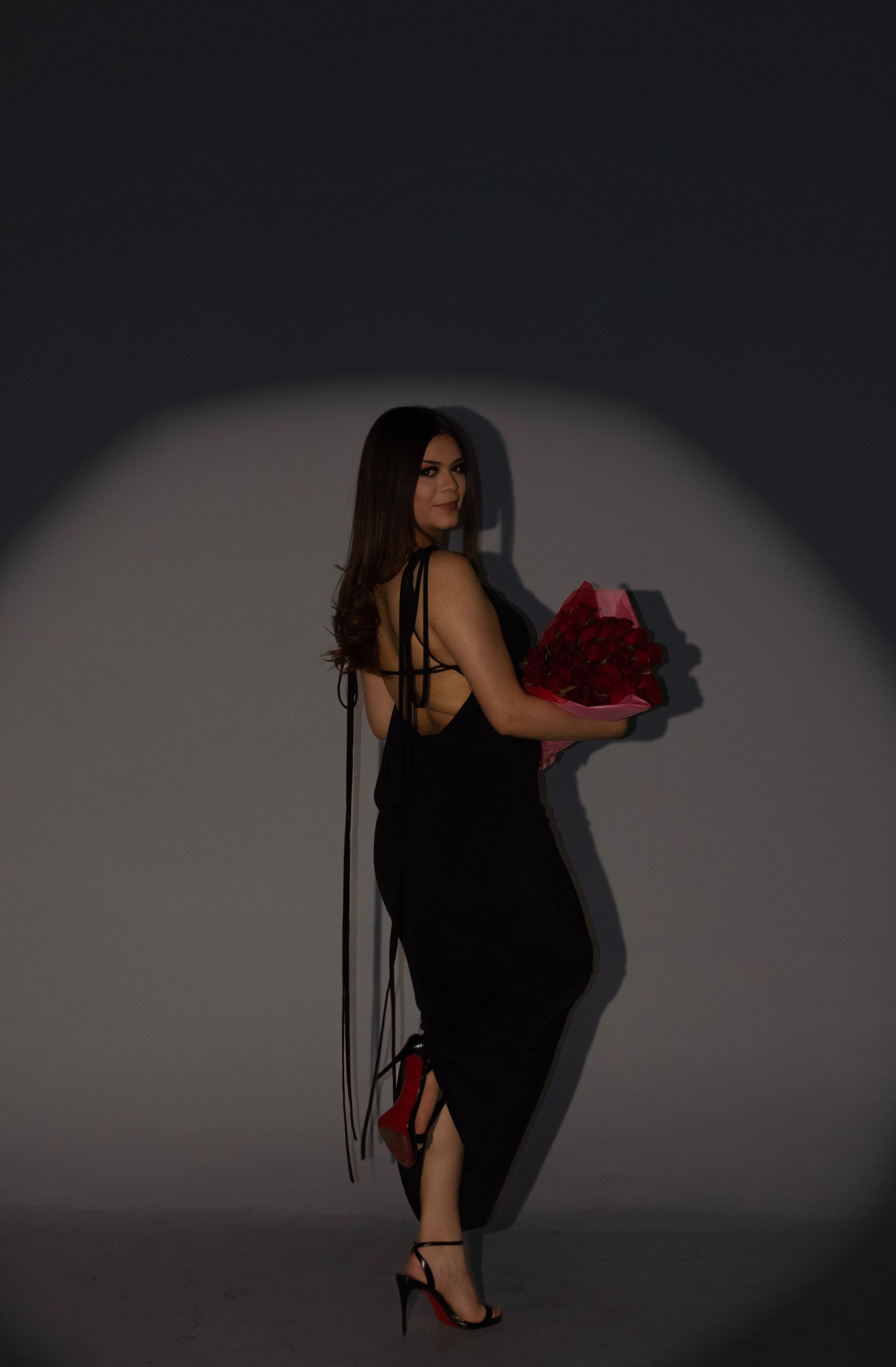 A woman in a black dress is holding a bouquet of red roses.