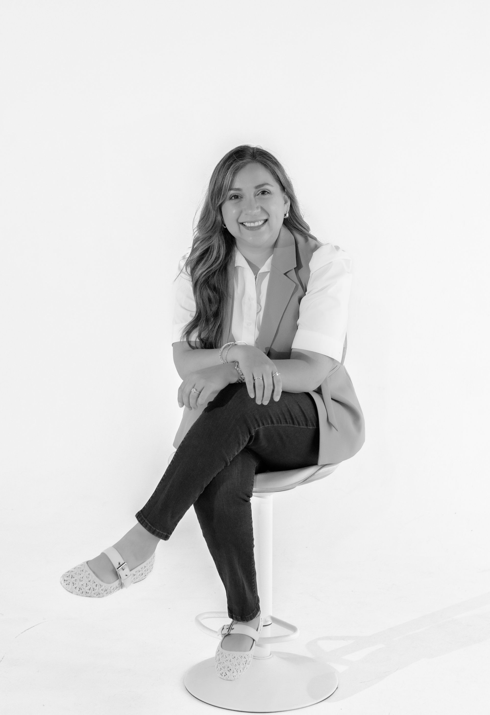 A woman is sitting on a chair with her legs crossed and smiling.