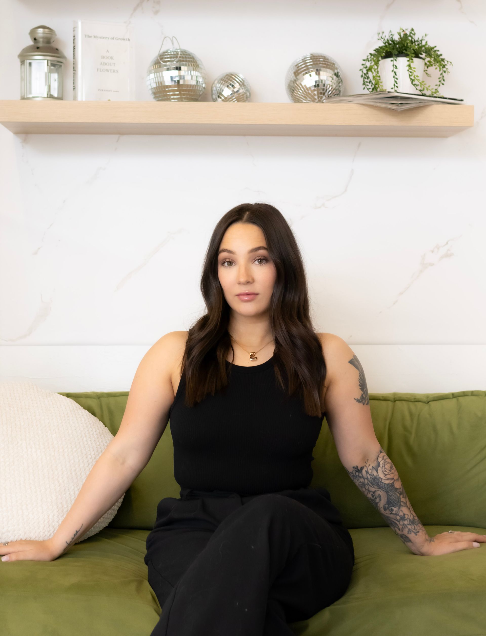 A woman with tattoos is sitting on a green couch.