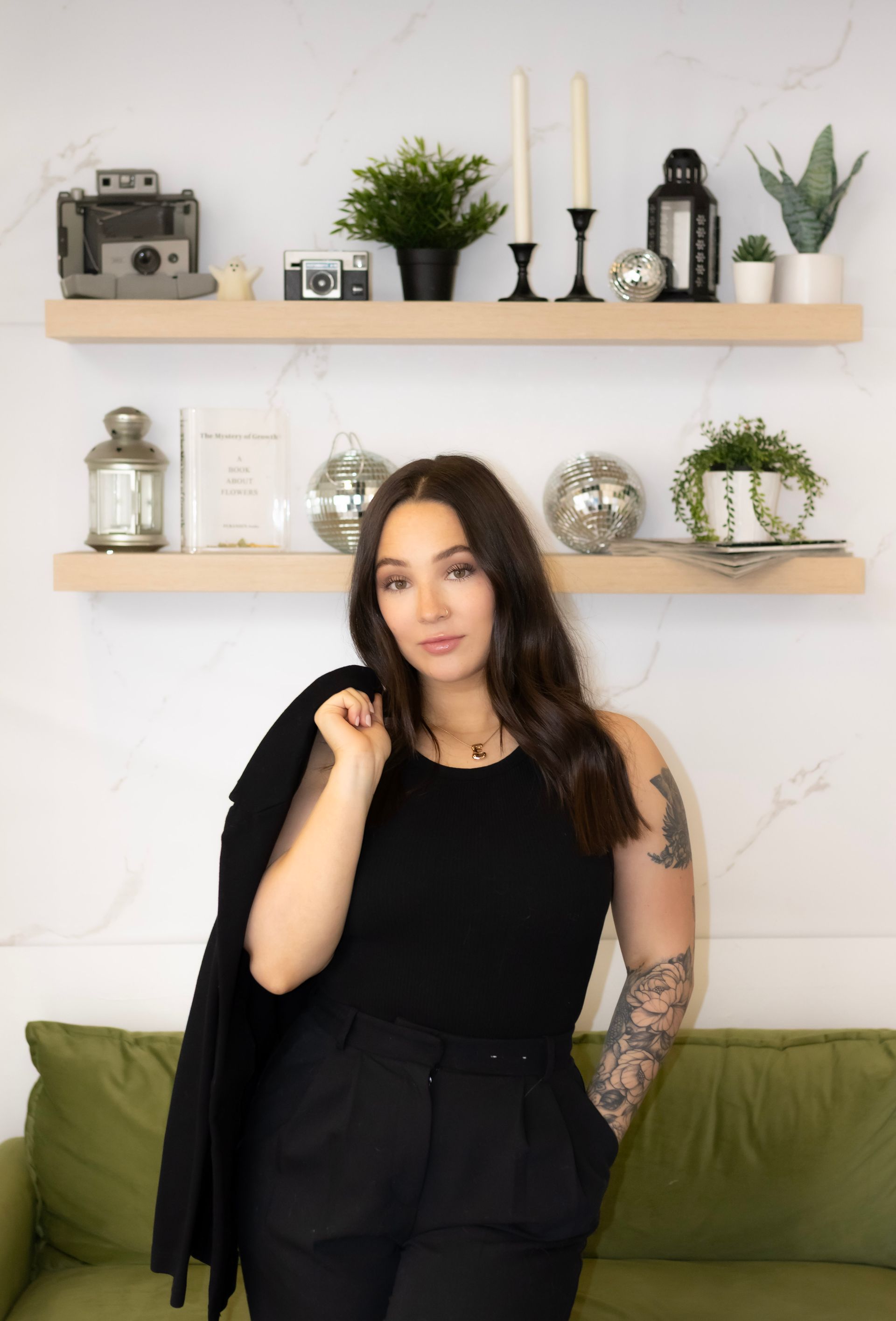 A woman in a black tank top and black pants is standing next to a green couch.