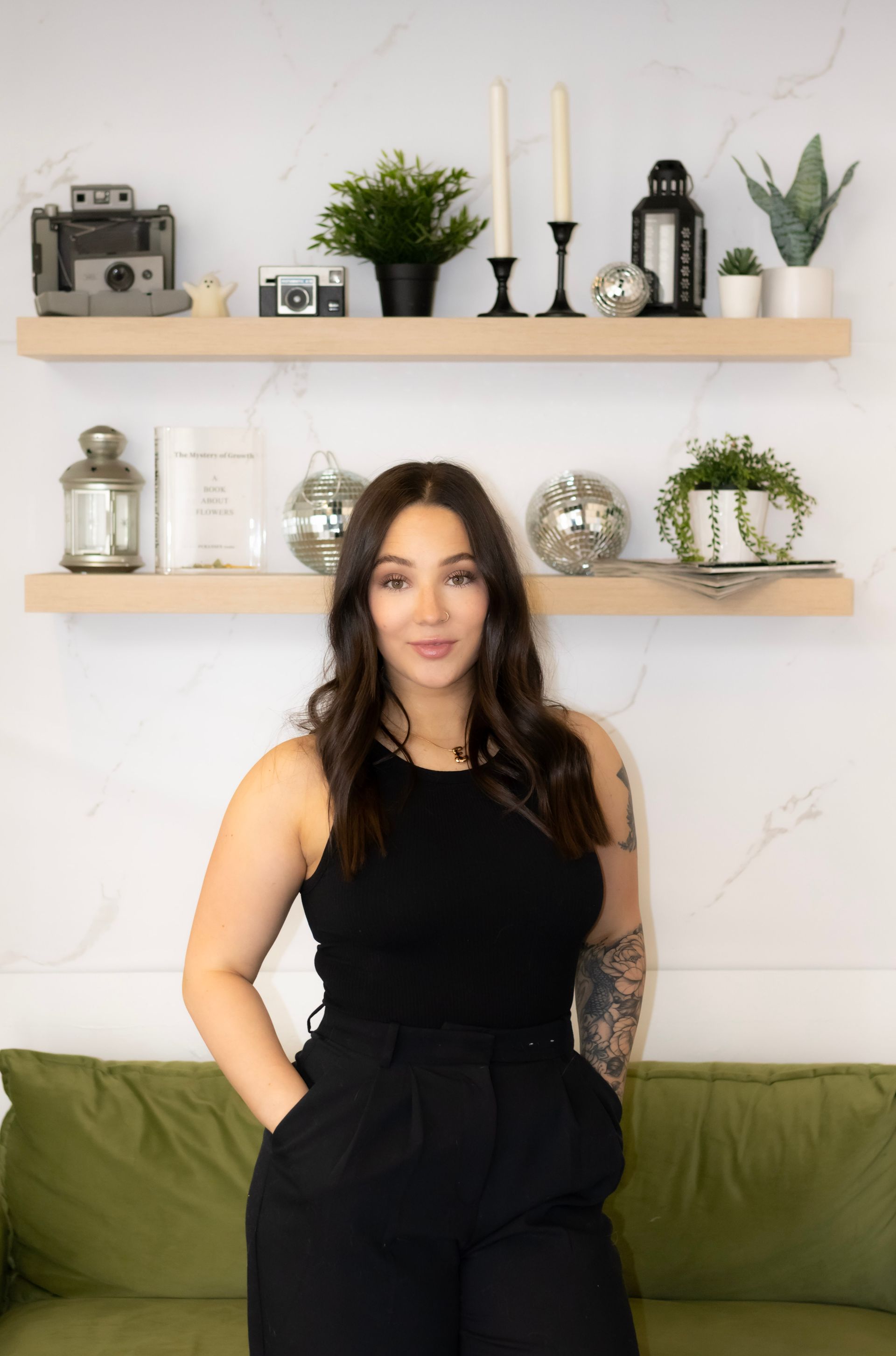 A woman in a black tank top and black pants is standing next to a green couch.