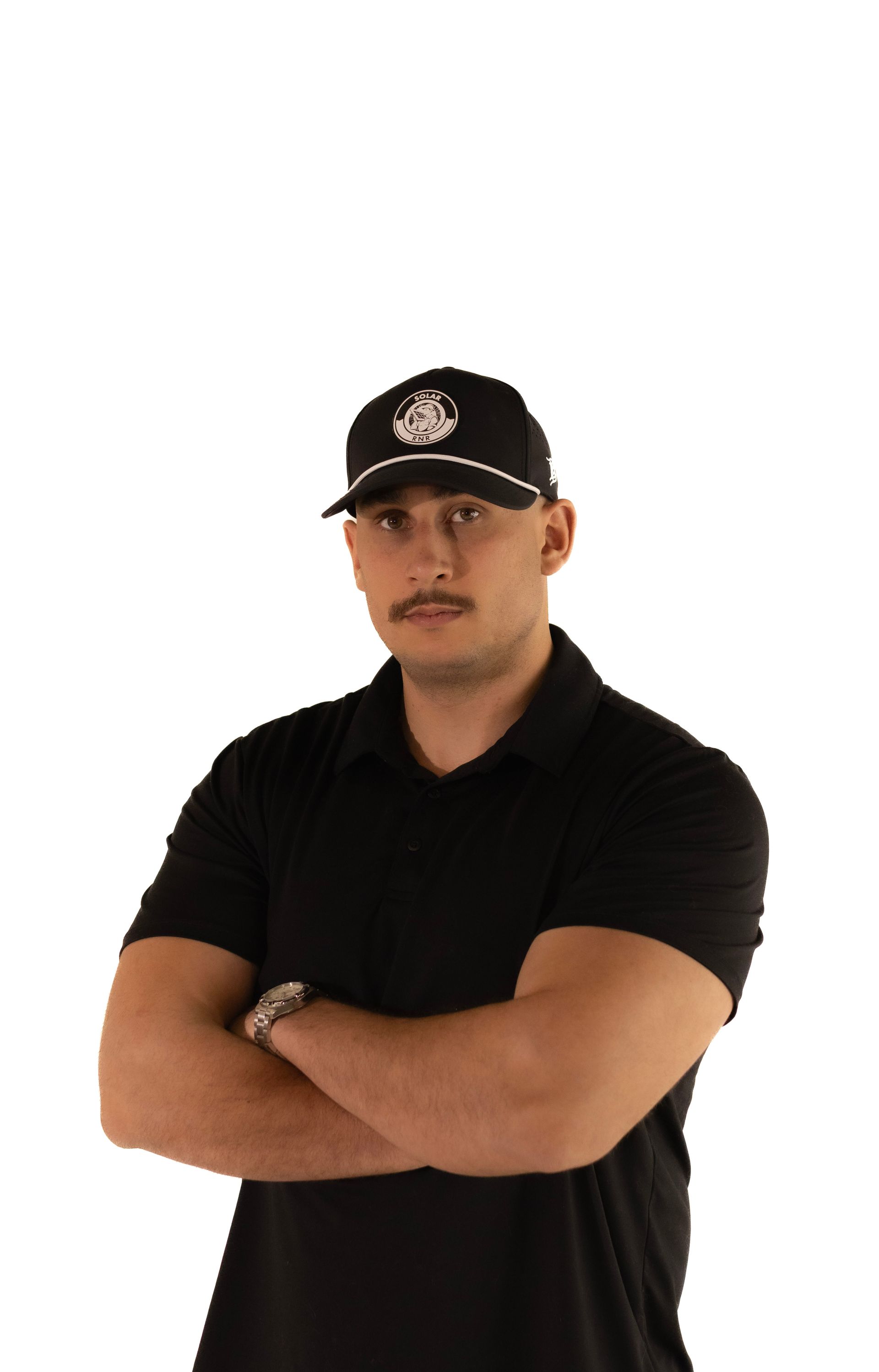 A man wearing a hat and a black shirt is standing with his arms crossed.
