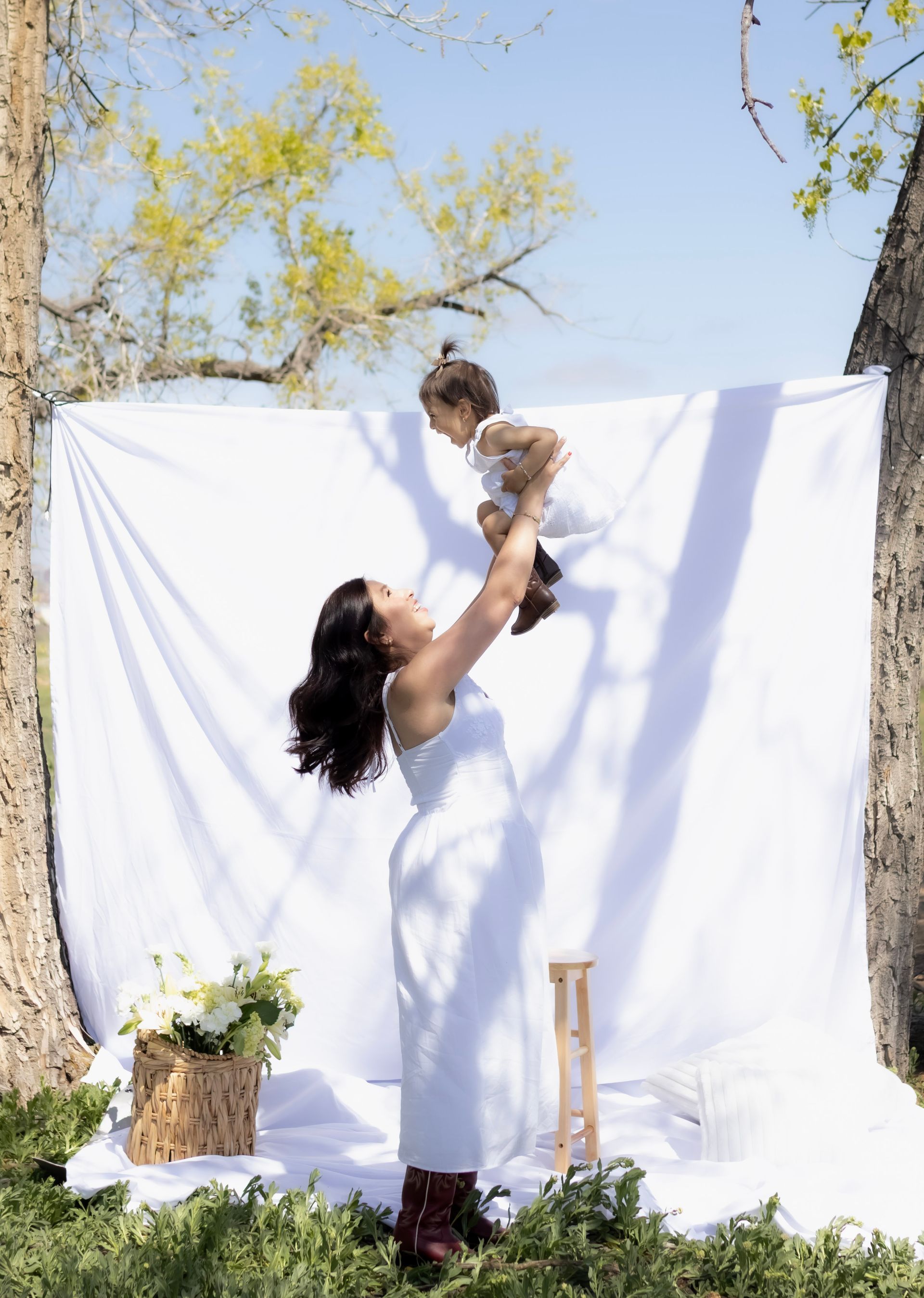A woman is holding a baby in her arms in front of a white cloth.