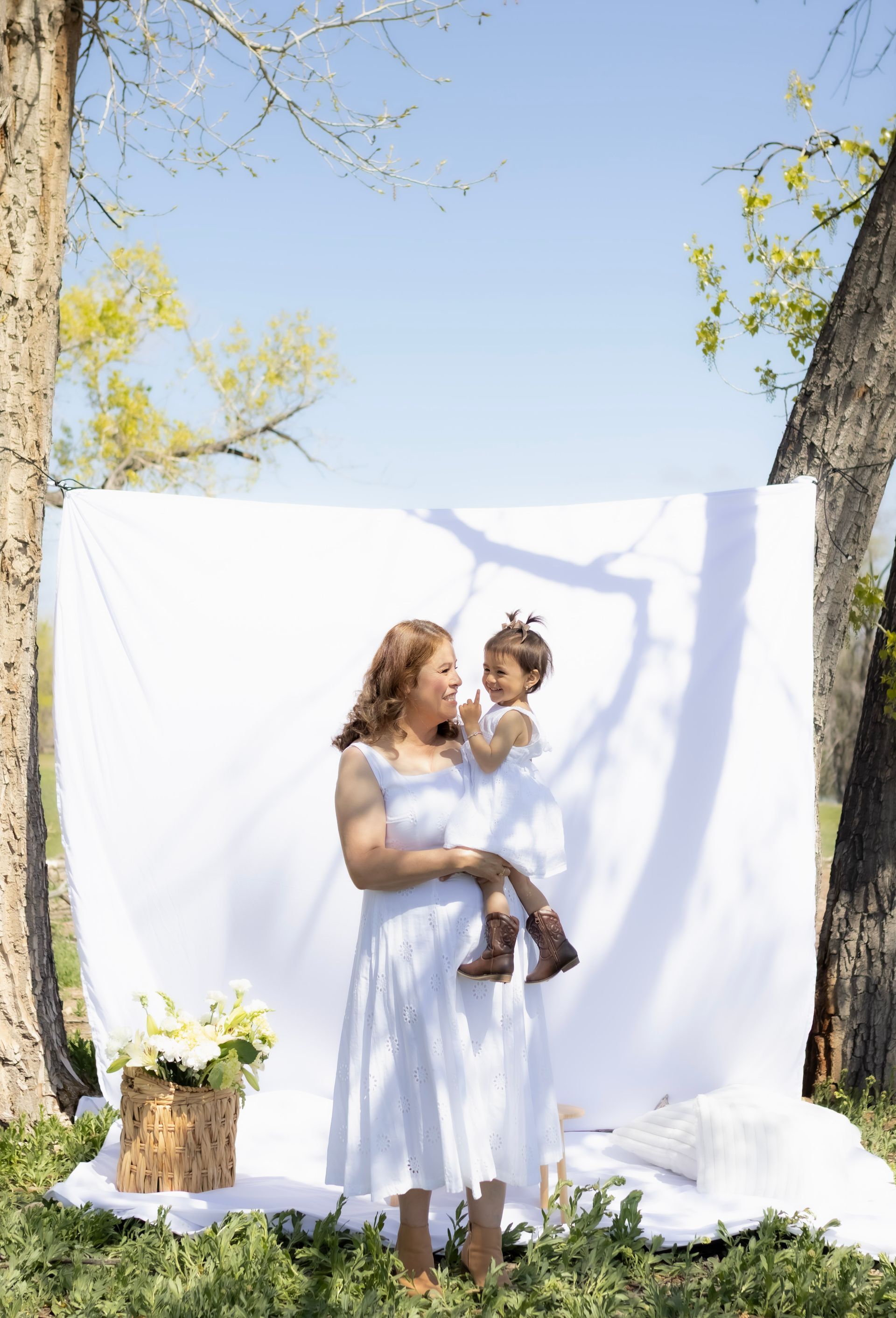 A woman in a white dress is holding a baby in front of a white cloth.