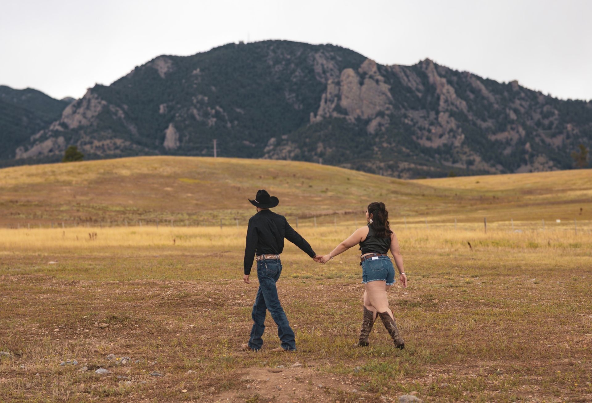A man and a woman are holding hands in a field with mountains in the background.