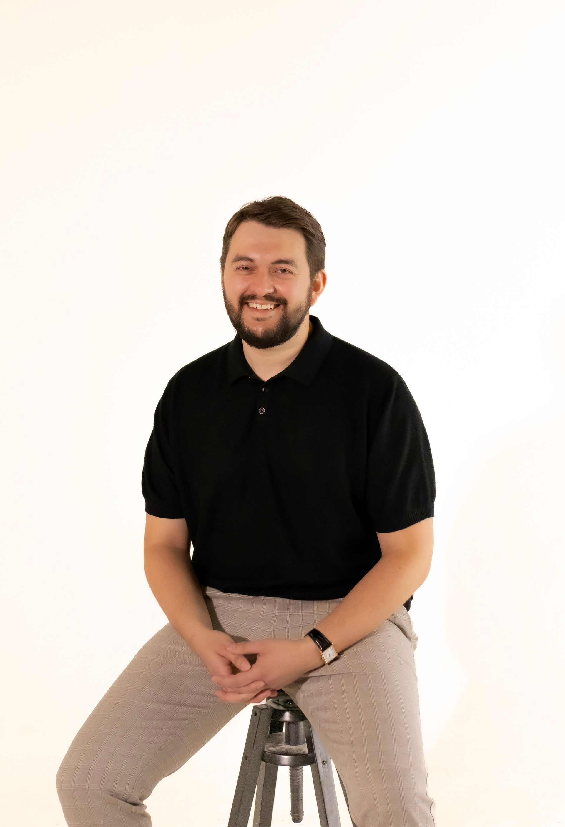 A man with a beard is sitting on a stool and smiling.
