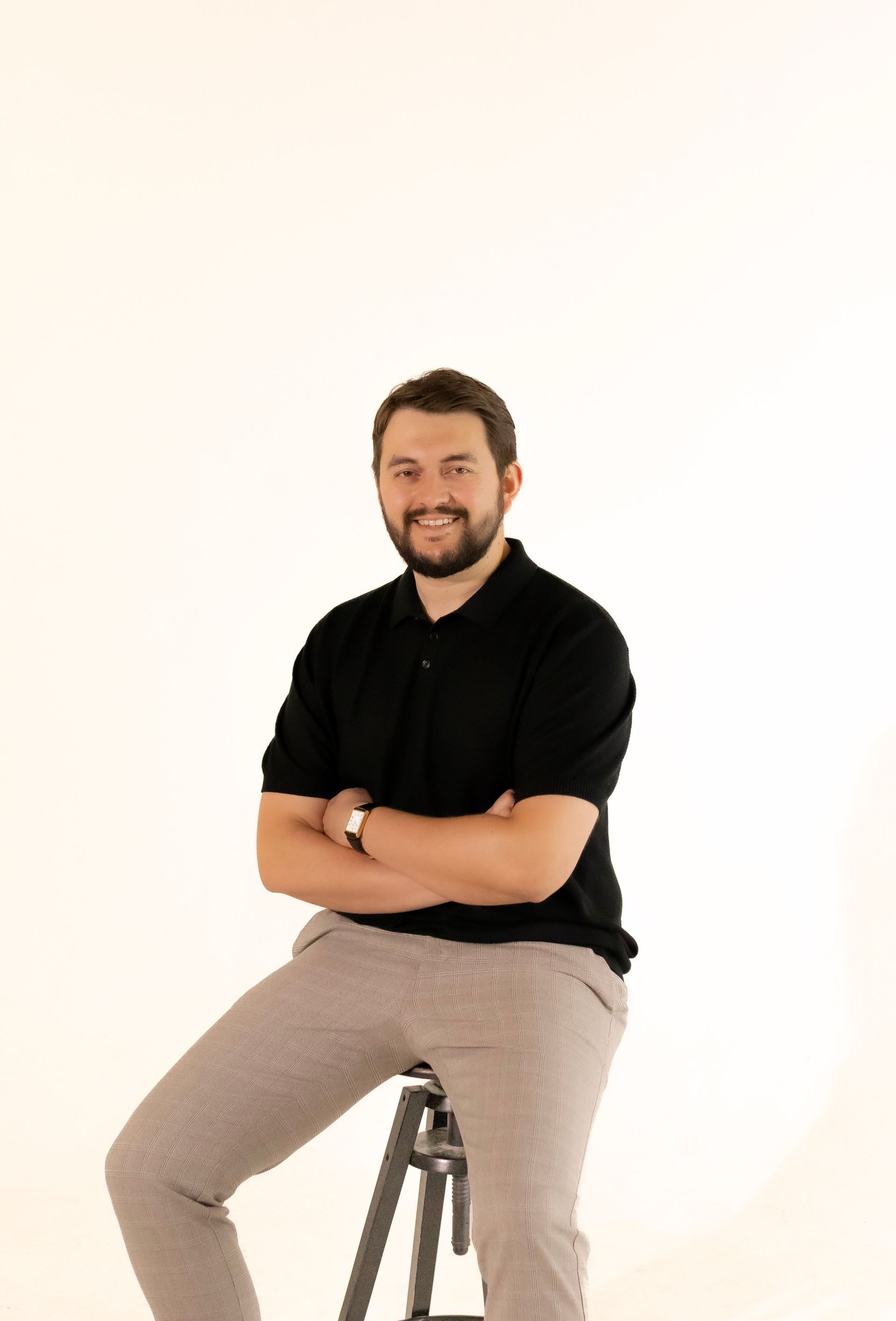 A man with a beard is sitting on a stool with his arms crossed.