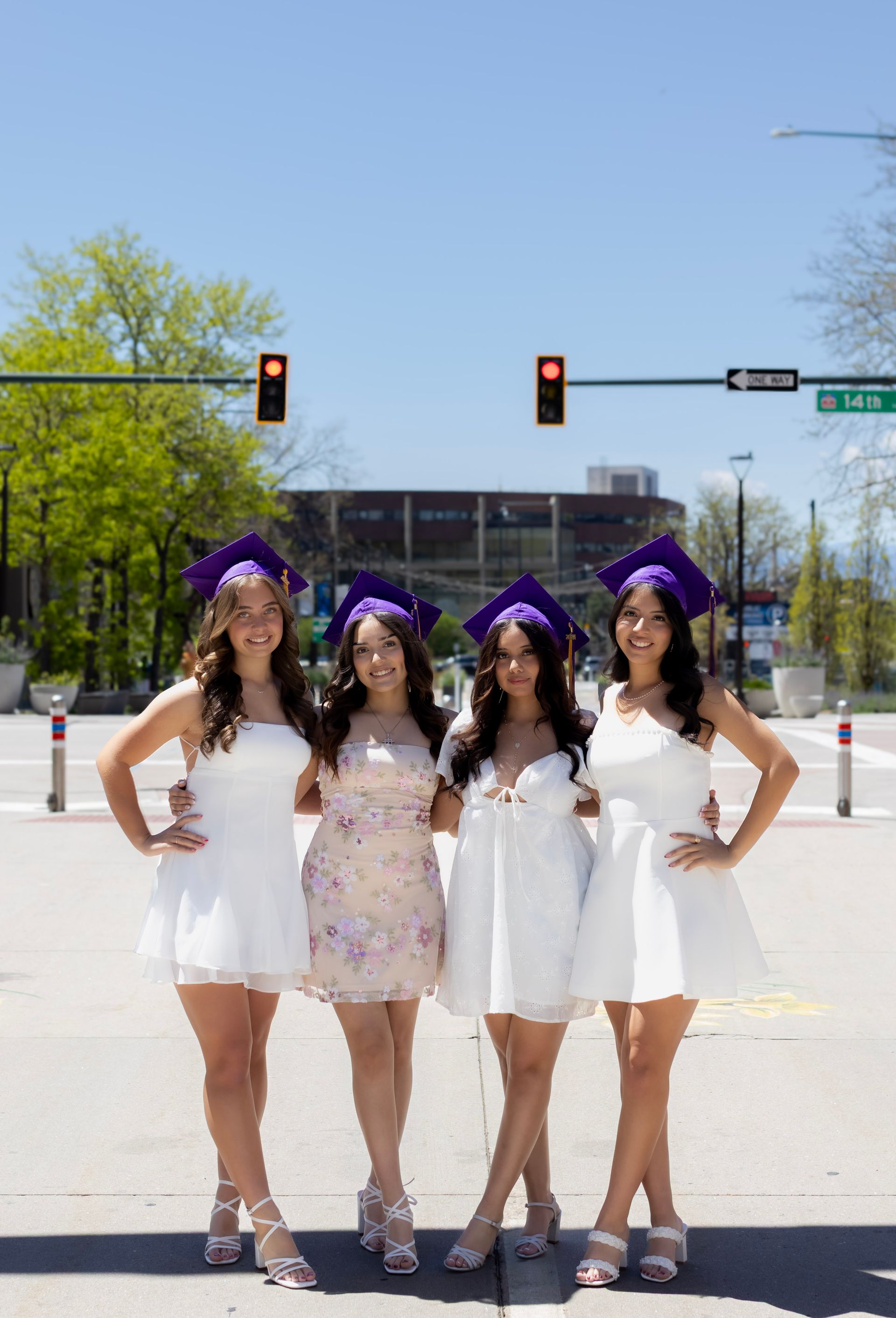 Four women in white dresses and purple graduation caps are posing for a picture.