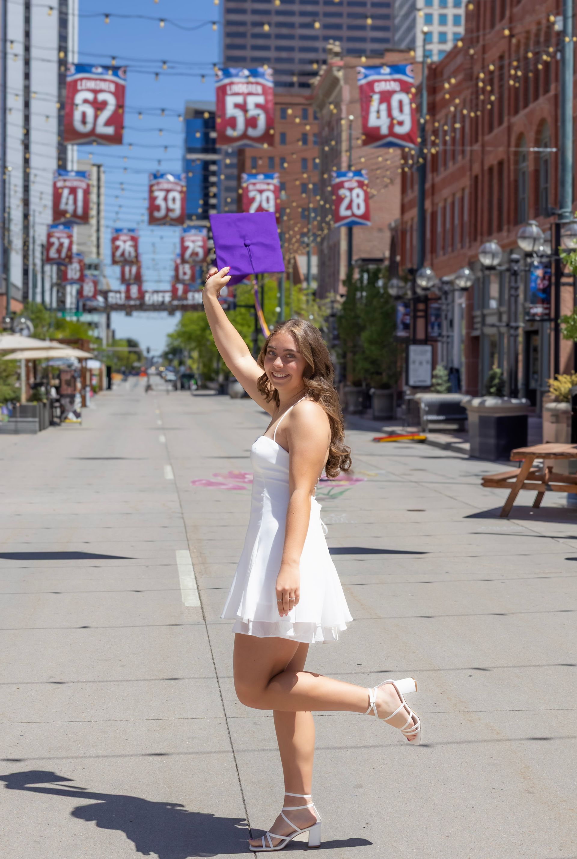A woman in a white dress is holding a purple graduation cap.