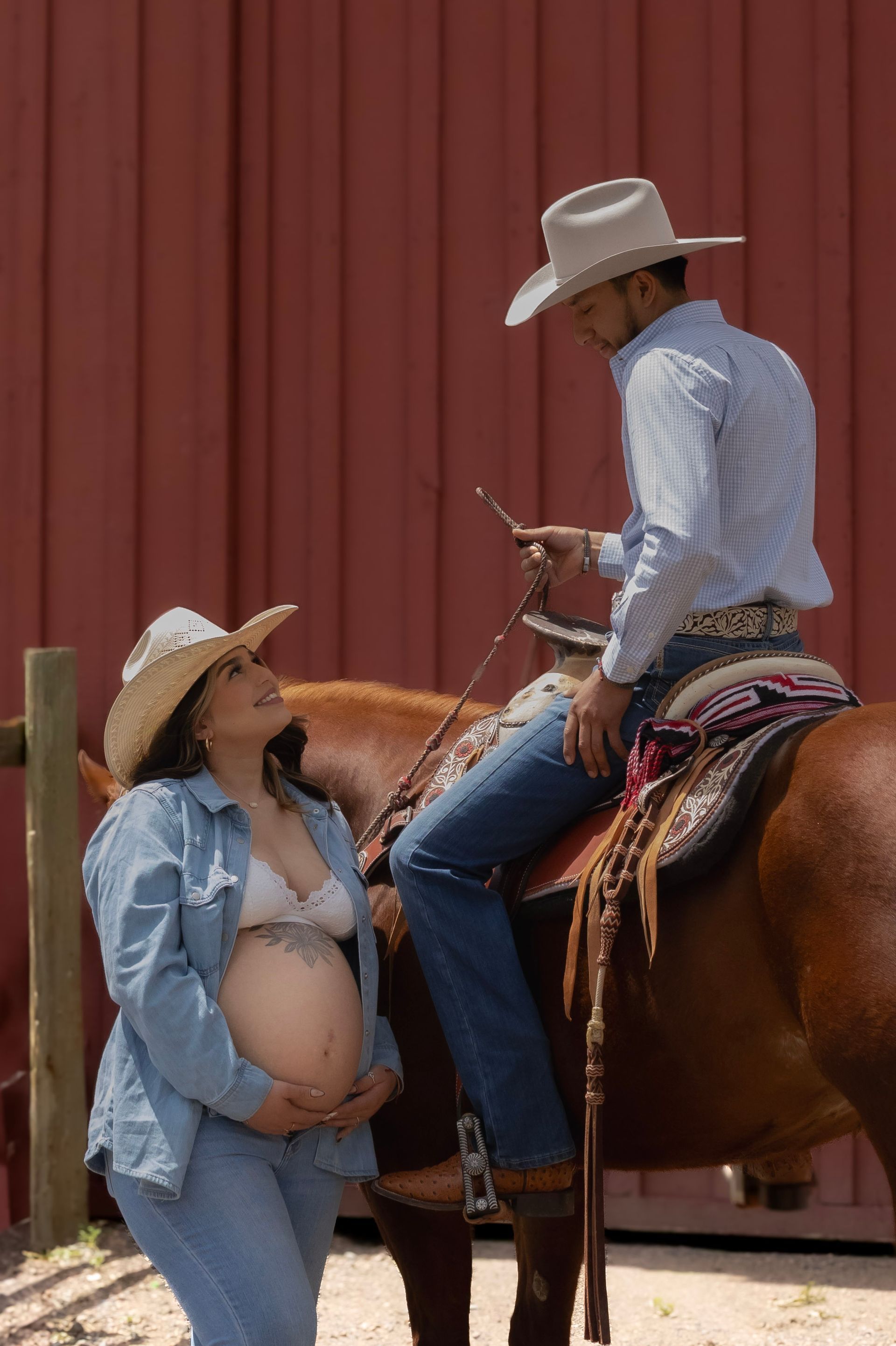 A pregnant woman is standing next to a cowboy on a horse.