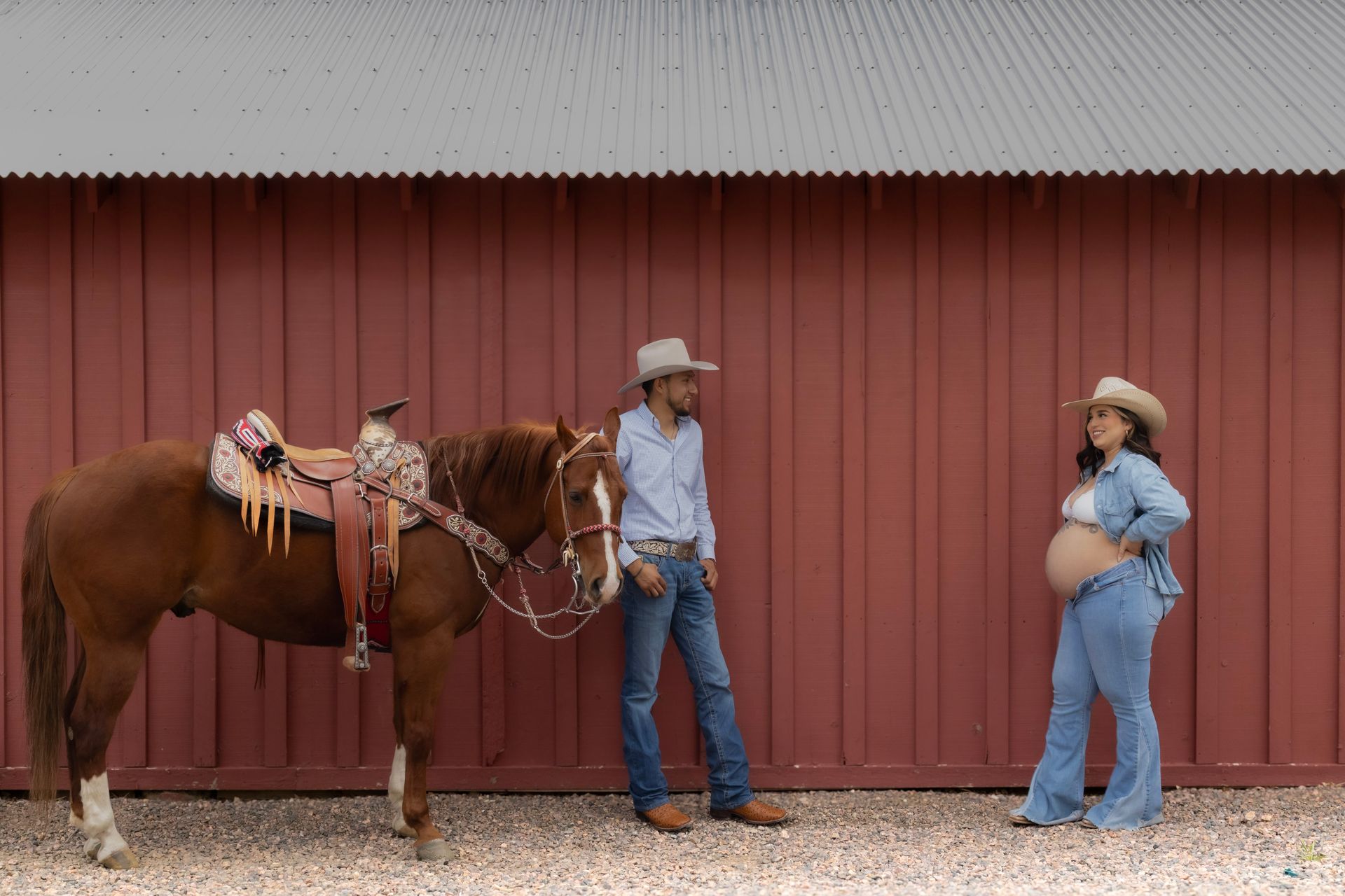 A man and a pregnant woman are standing next to a horse.