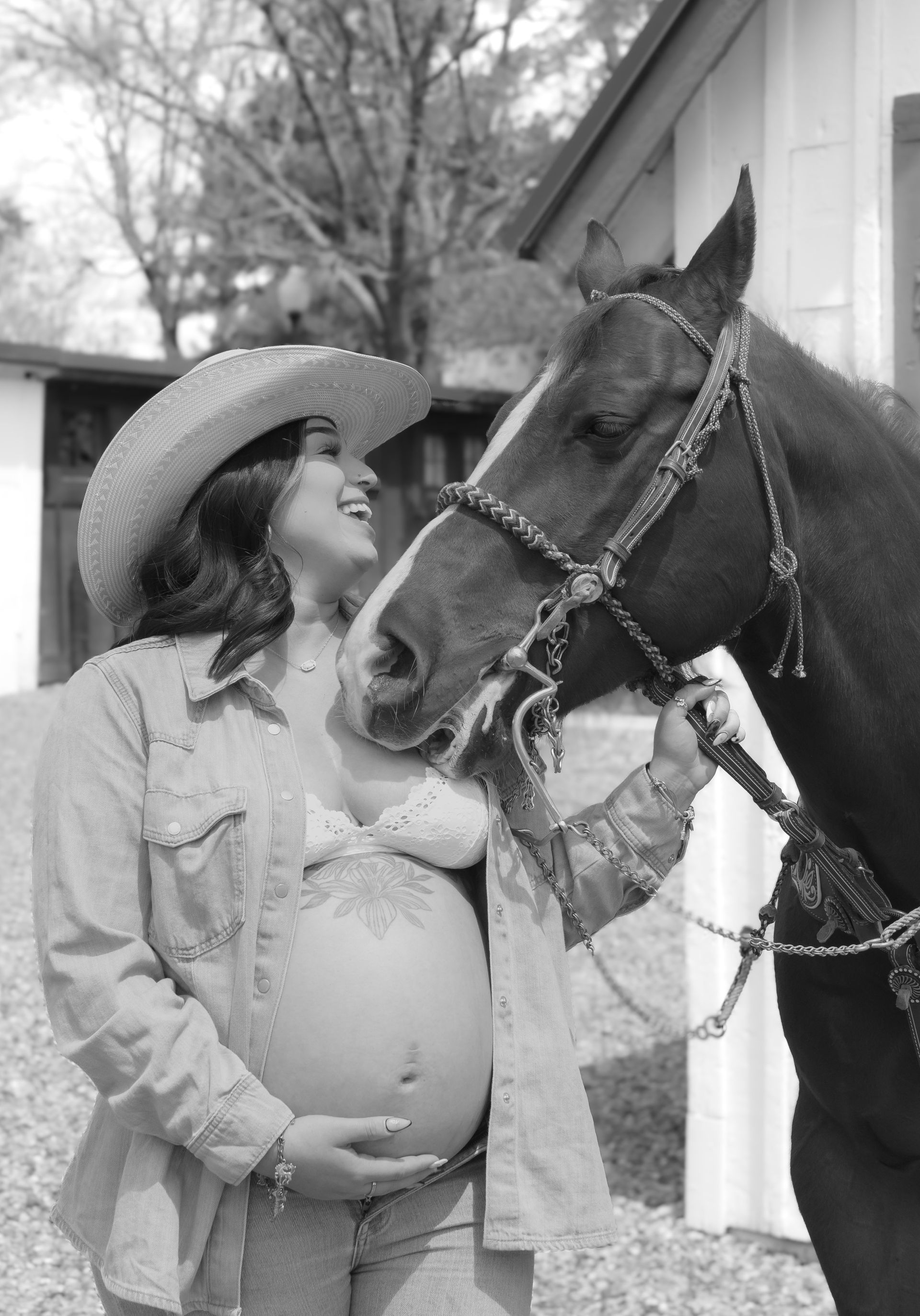 A pregnant woman in a cowboy hat is standing next to a horse