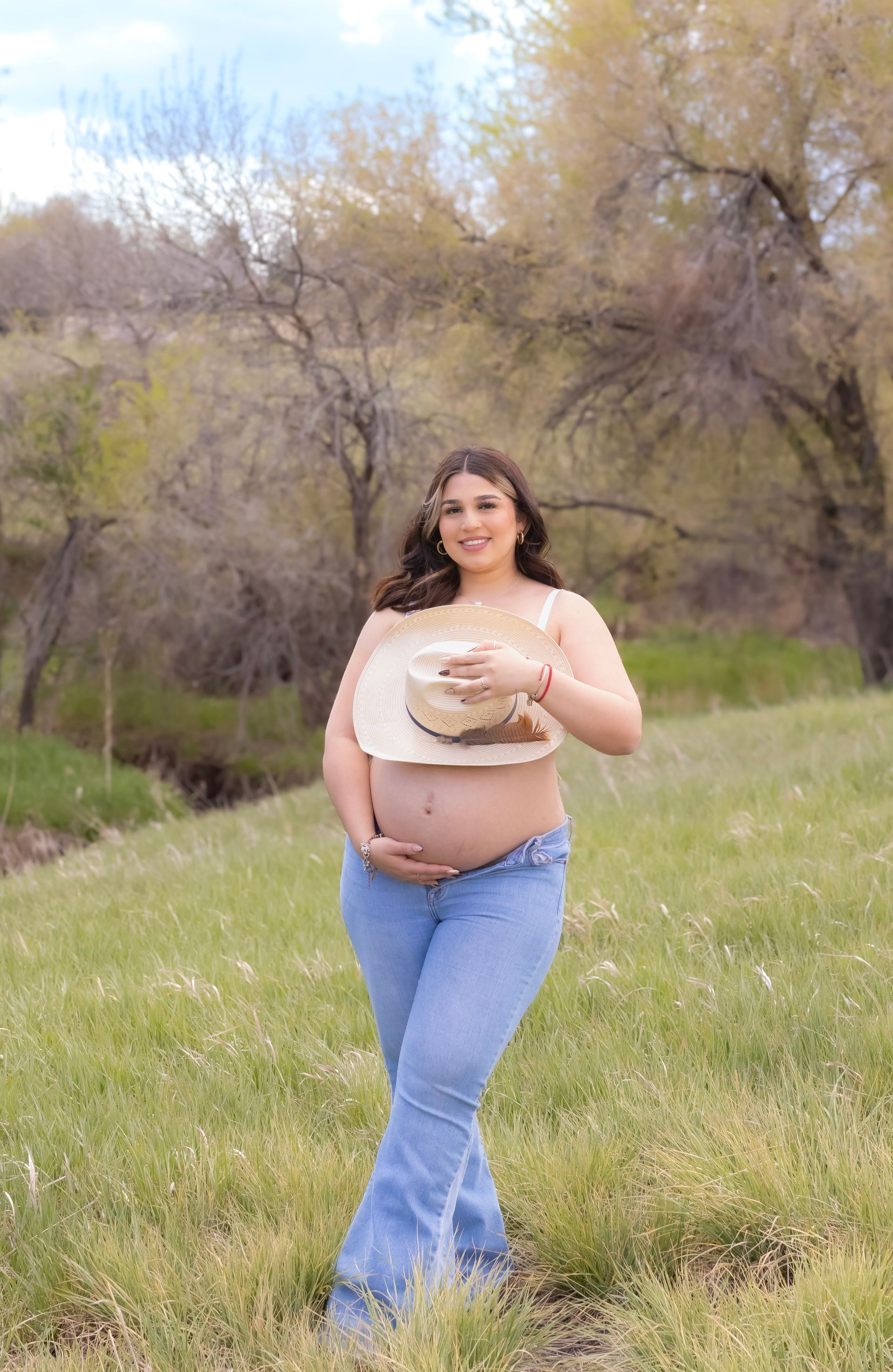 A pregnant woman wearing a cowboy hat is standing in a field.