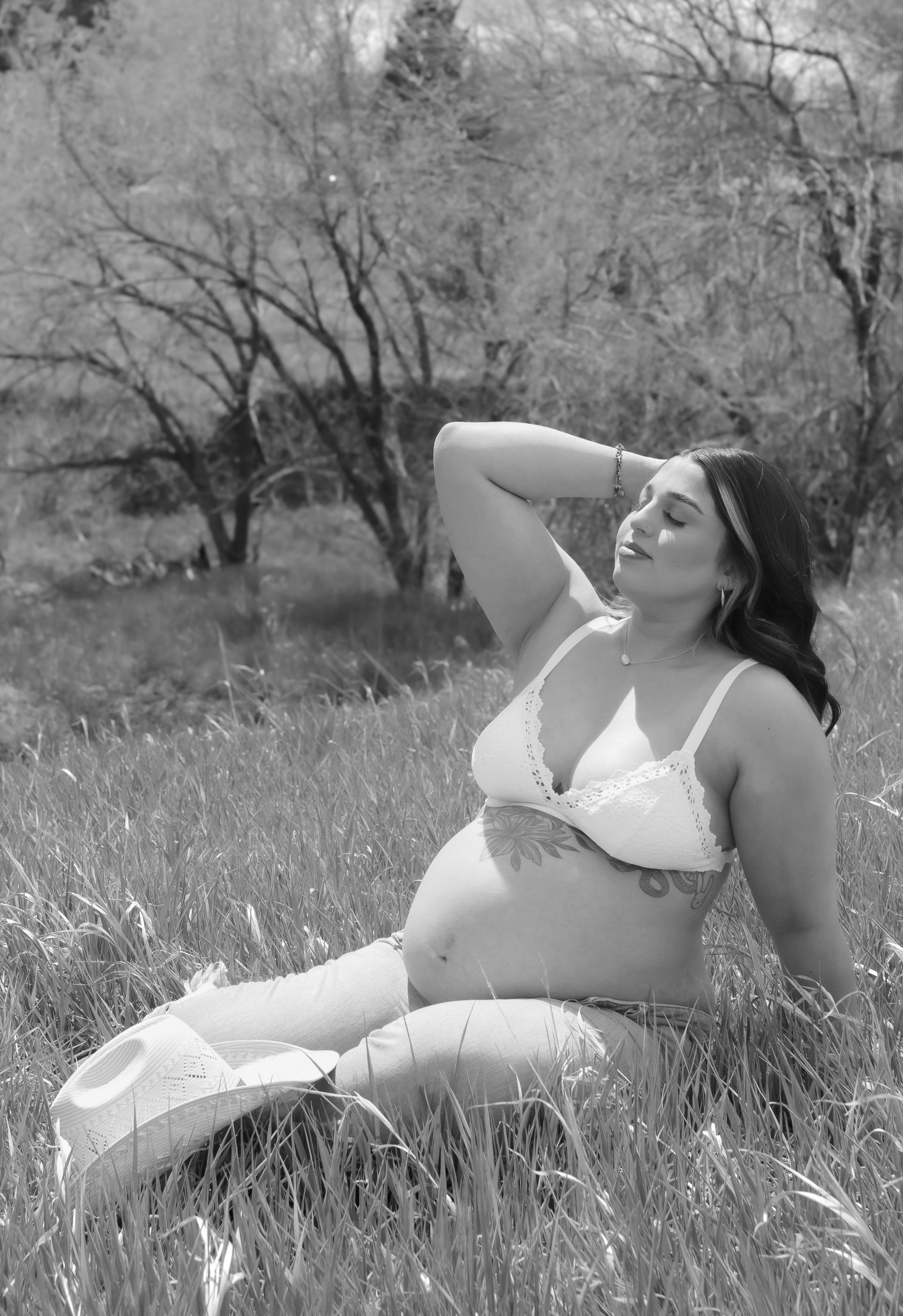 A black and white photo of a pregnant woman sitting in a field.