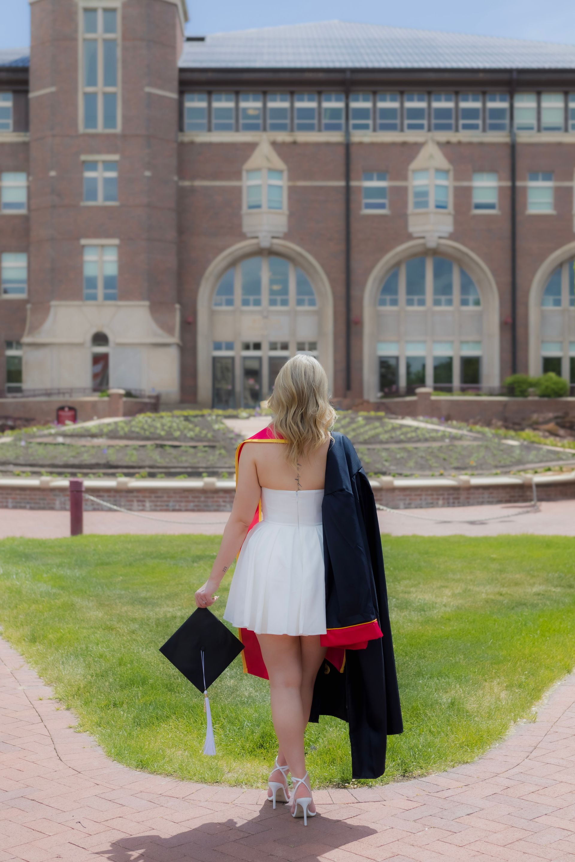 A woman in a graduation cap and gown is standing in front of a large building.