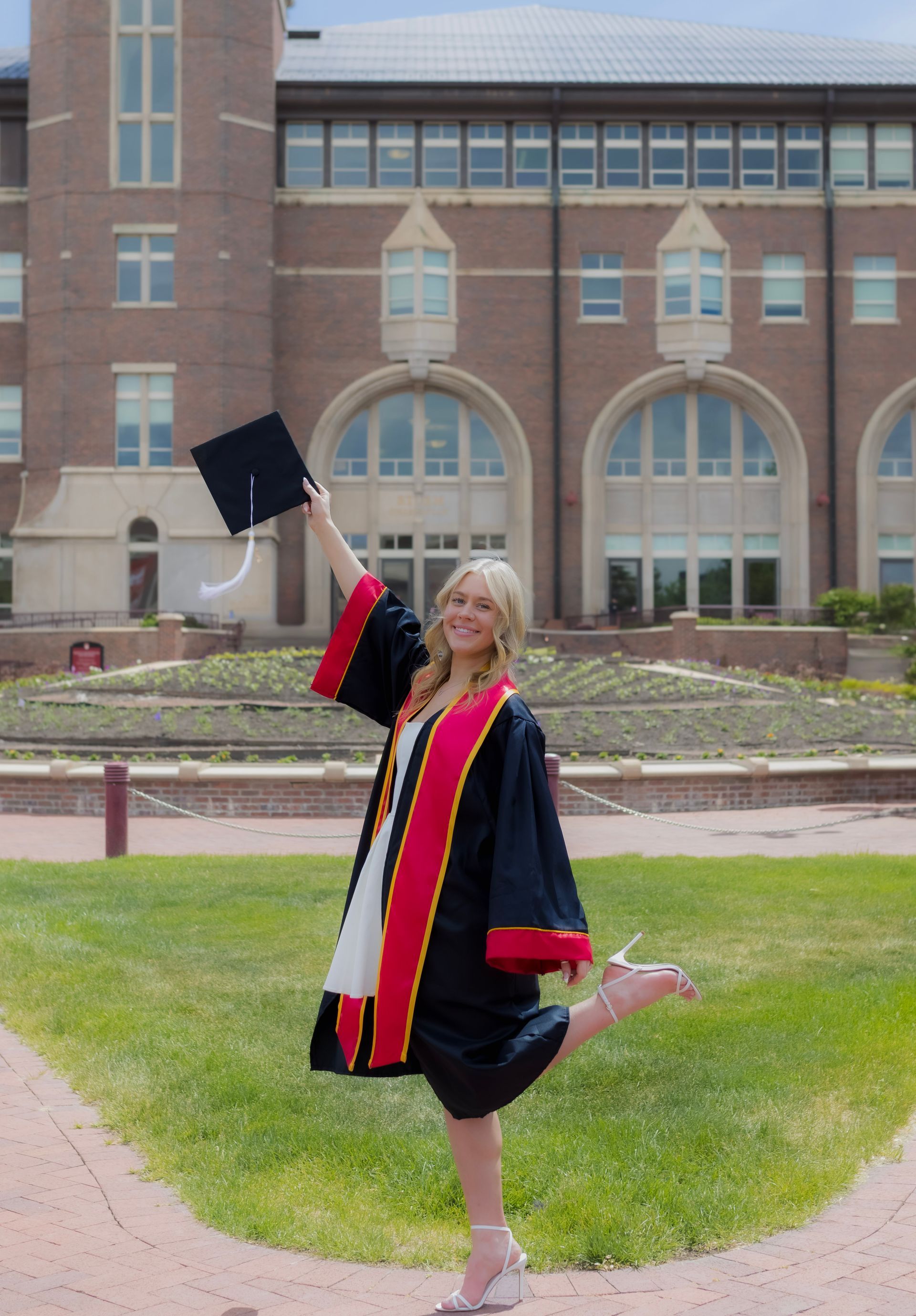 A woman in a graduation cap and gown is holding her cap in the air