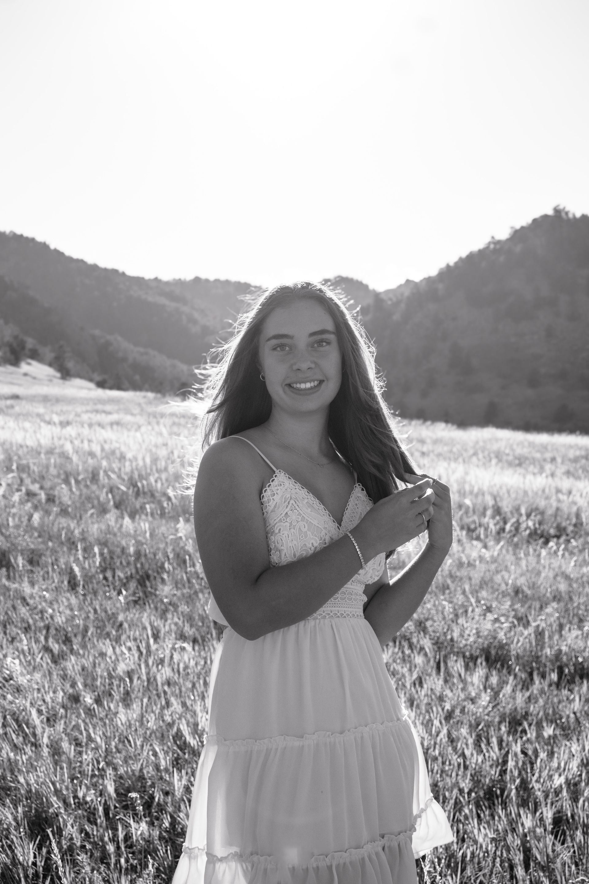 A woman in a white dress is standing in a field with mountains in the background.