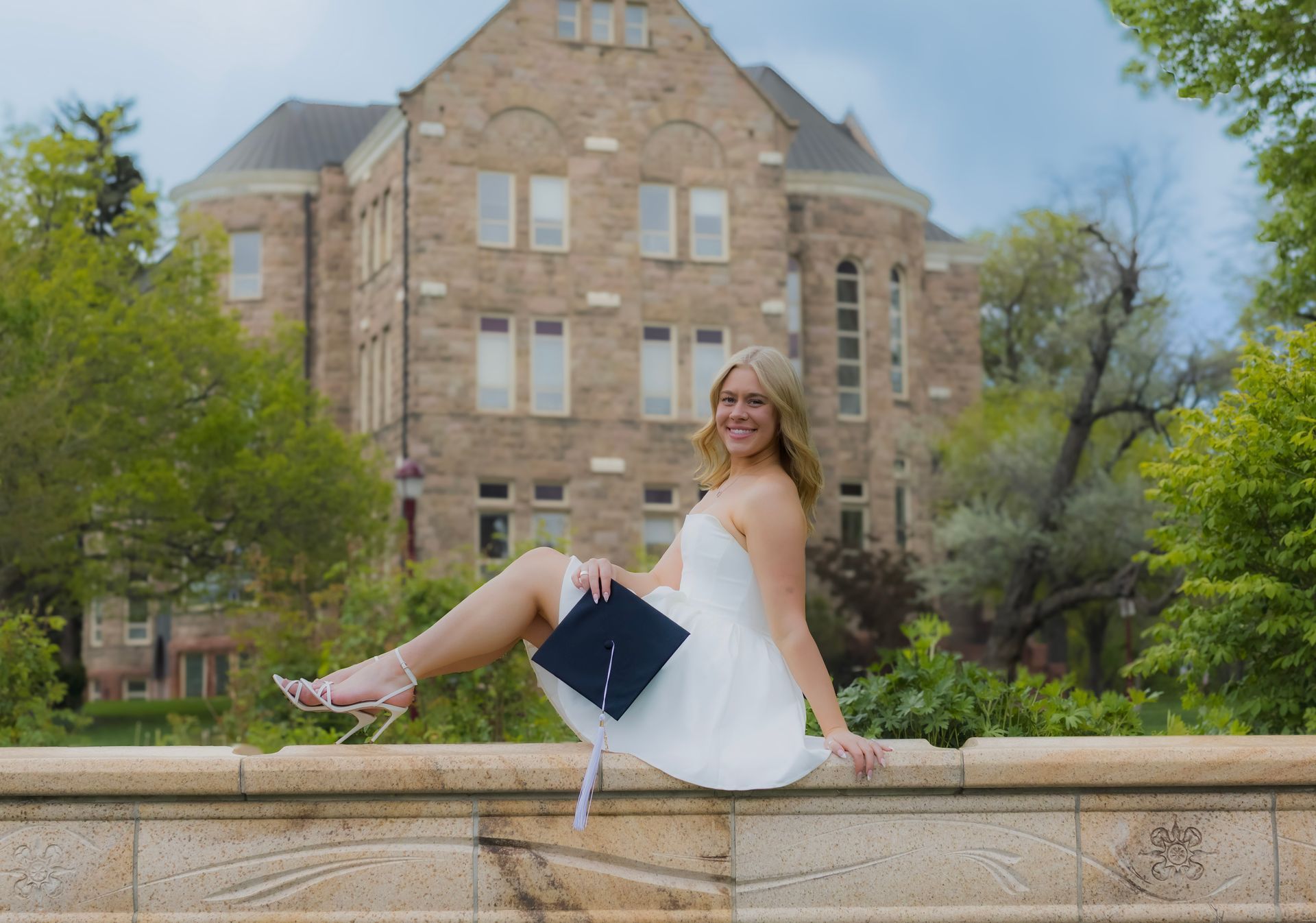 A woman in a white dress is sitting on a wall with her legs crossed.