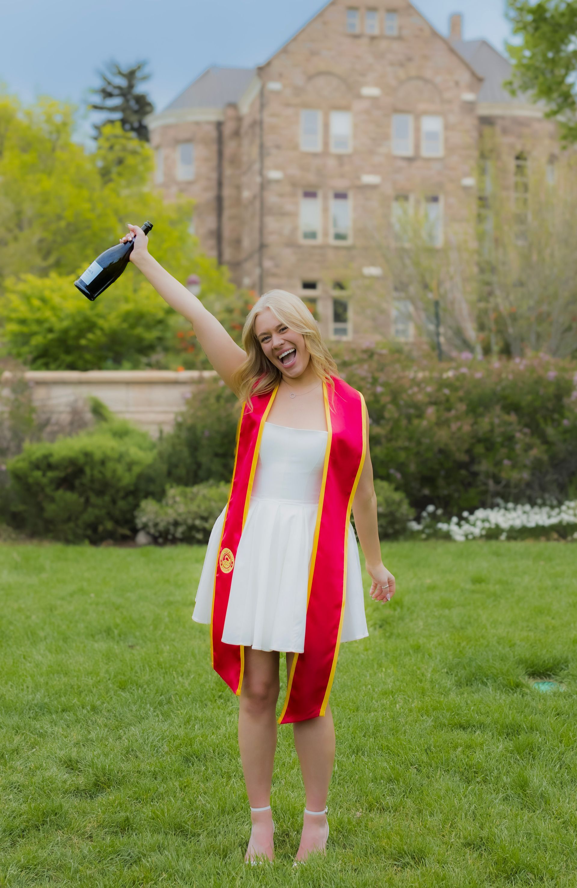 A woman in a graduation cap and gown is holding a bottle of champagne in her hand.