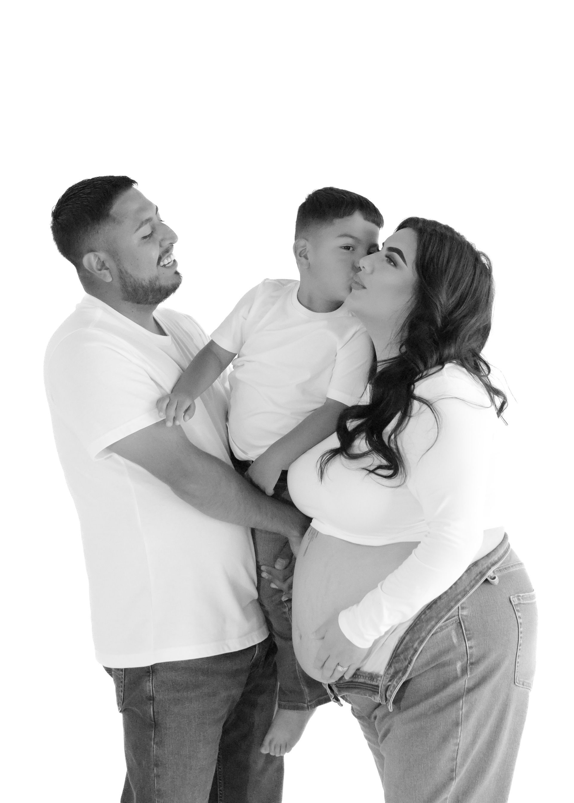 A black and white photo of a pregnant woman kissing her husband and son.