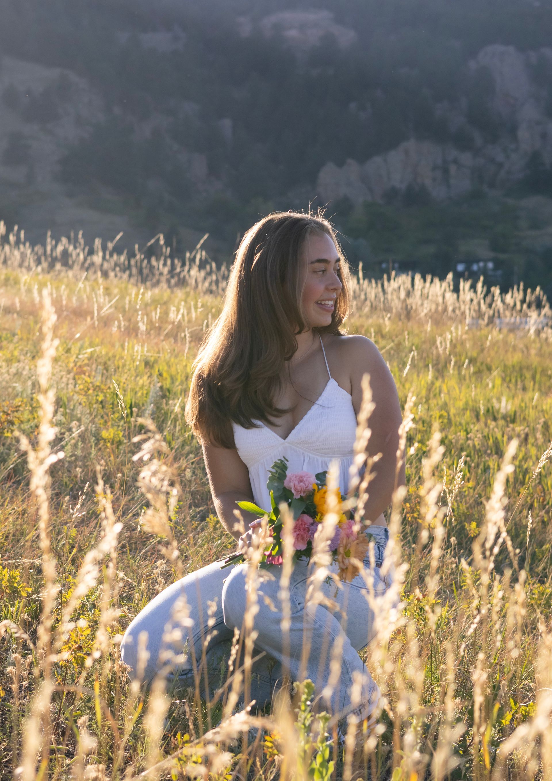 A woman is kneeling in a field of tall grass holding a bouquet of flowers.