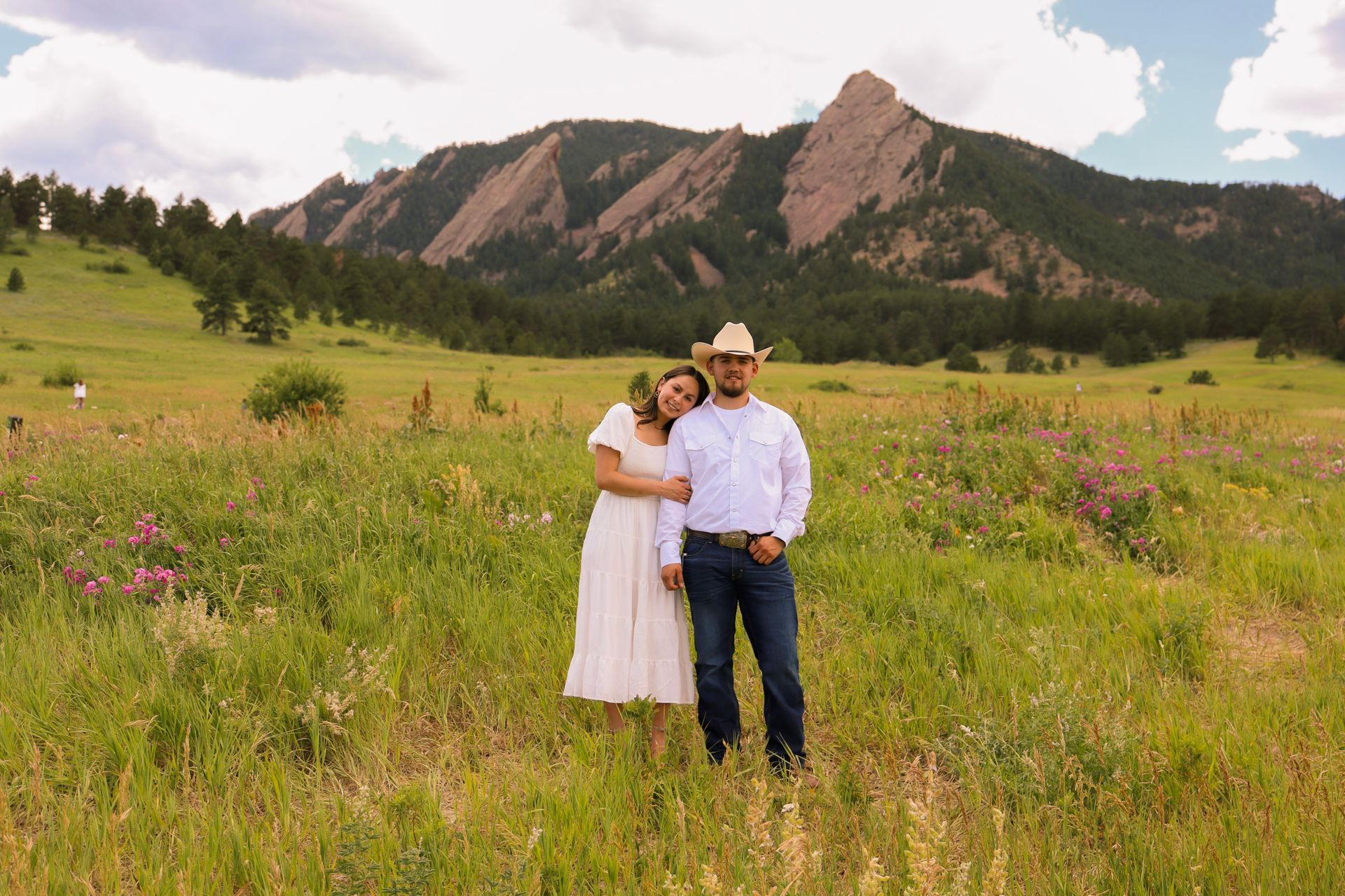 A man and a woman are standing in a field with mountains in the background.